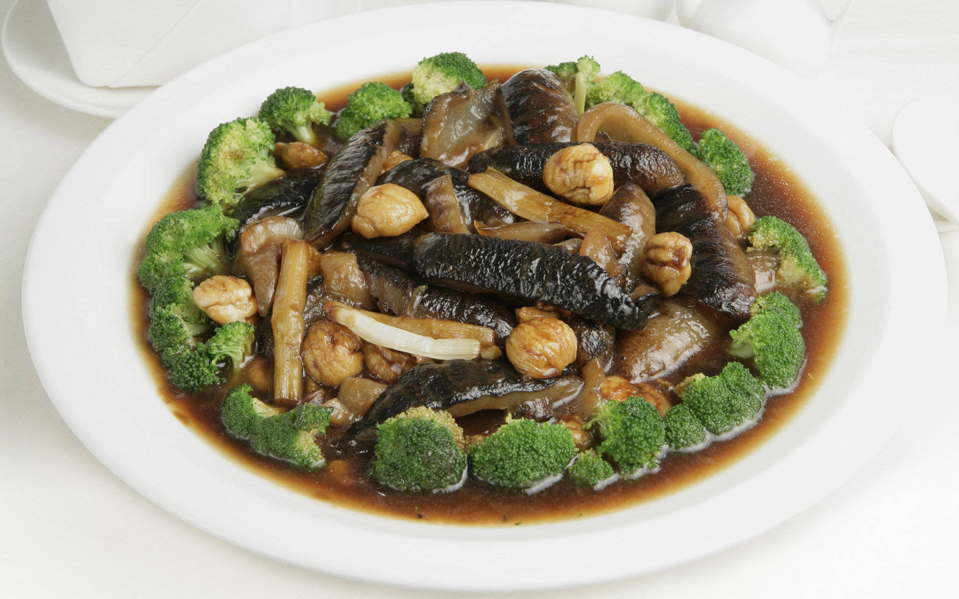 4K Food 桌布 壁紙 — 一盤光澤的炒菜，有花椰菜、腰果和深色蘑菇，配上濃郁的棕色醬汁，盛在白盤上。