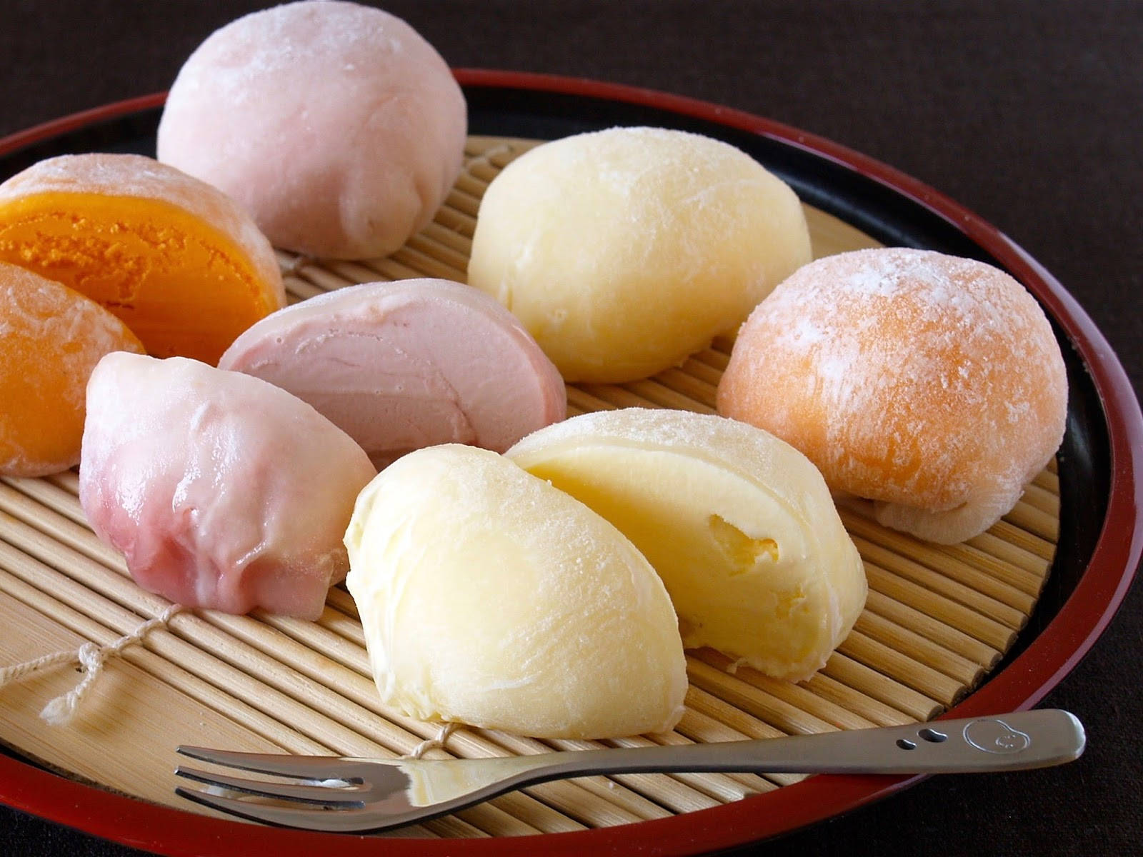 Mochi 桌布 壁紙 — 一盤各種粉紅、黃色和橙色色調的柔軟麻糬糰子，撒上糖粉，放在竹蓆上。