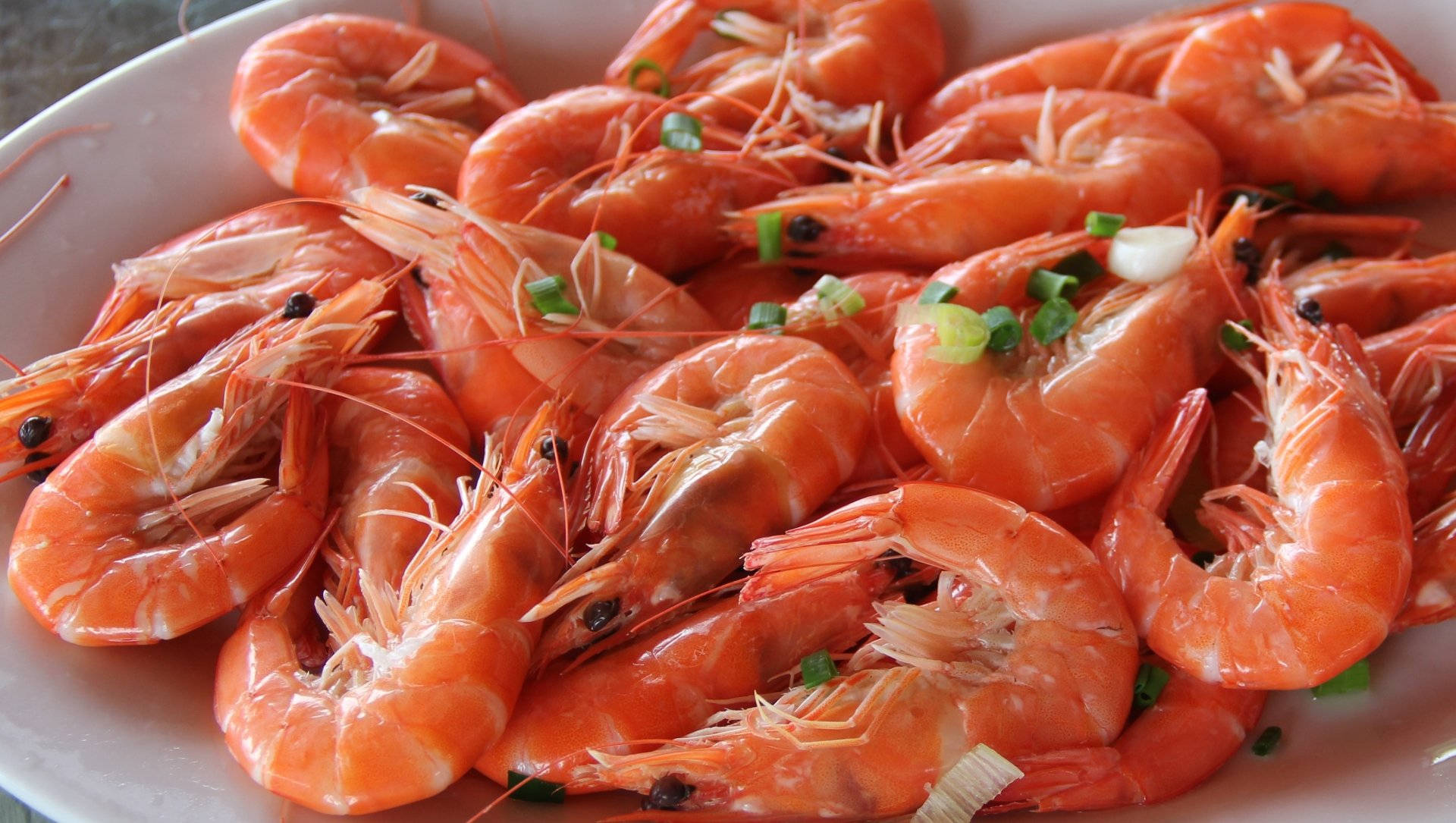 Seafood 桌布 壁紙 — 一盤堆得高高的鮮橙色熟蝦，飾以切碎的青蔥和黑胡椒粒。