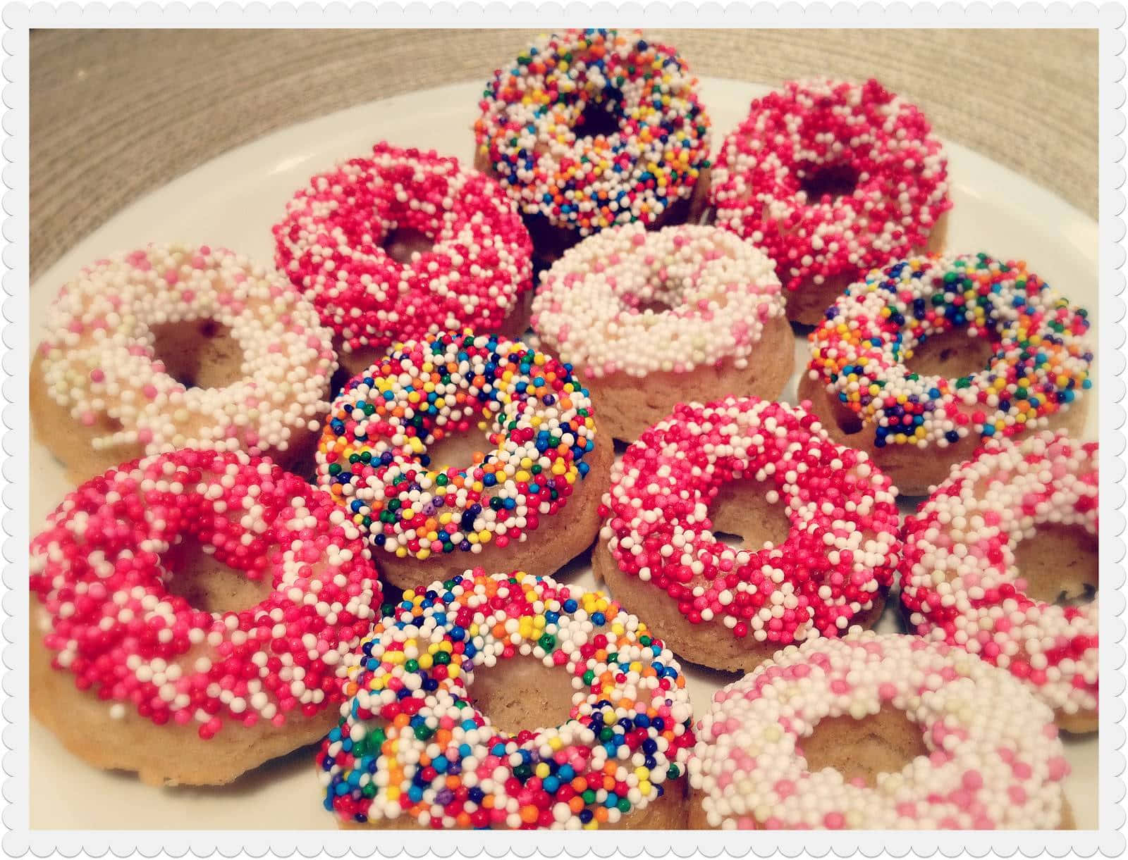 donuts 桌布 壁紙 — 一盤堆滿粉紅、白色和彩虹色繽紛糖霜甜甜圈。