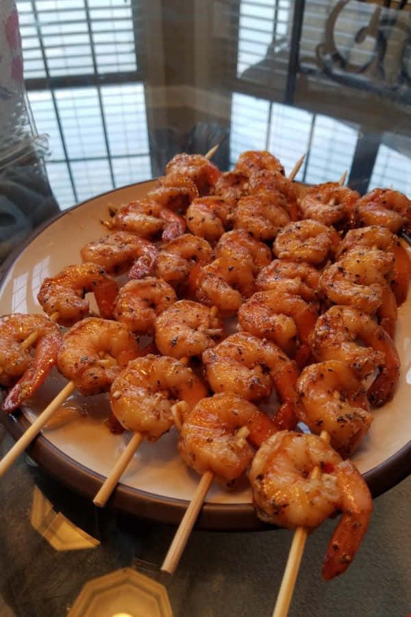Delicious Food 桌布 壁紙 — 一盤堆滿金黃色烤蝦串，閃爍著調味料和醬汁的光澤。
