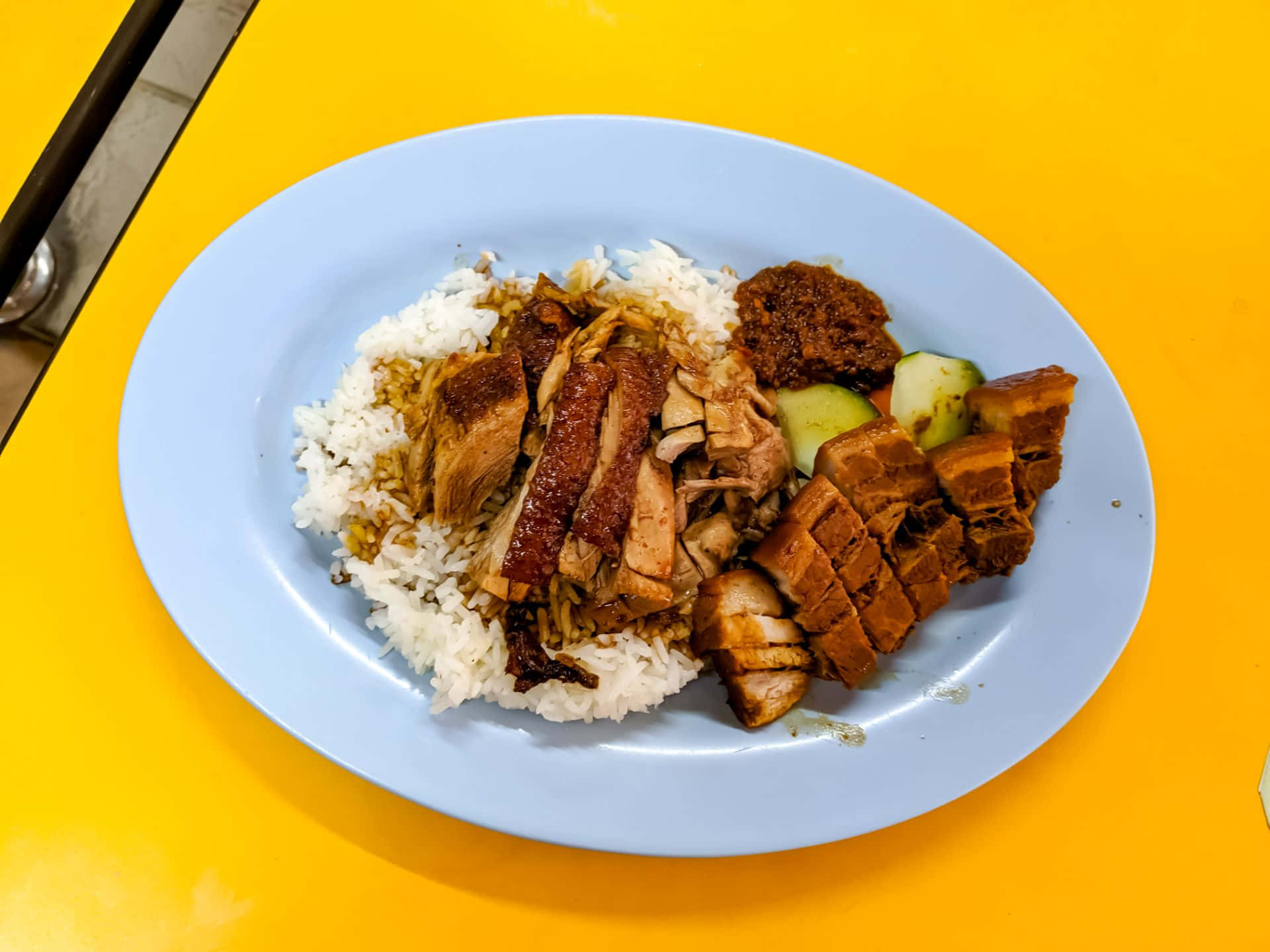 Food Photography 桌布 壁紙 — 一盤多汁的烤肉和米飯放在一張充滿活力的黃色桌子上，飾以小黃瓜和辣醬。