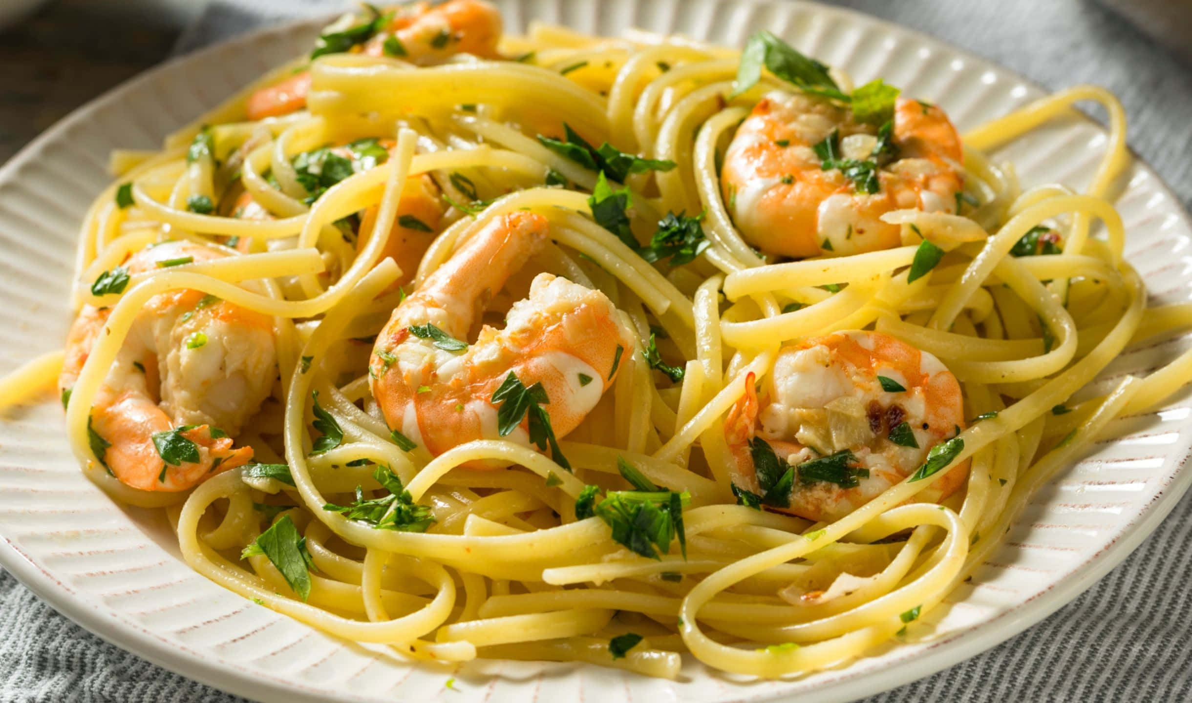 2440x1440 Pasta 桌布 壁紙 — 一盤奶油蒜香蝦義大利麵，飾以新鮮歐芹，盛載於紋理白色盤子上。