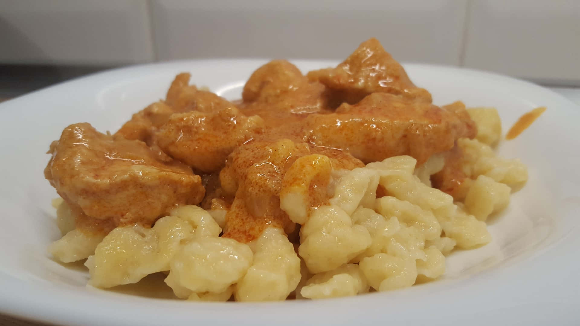 Chicken 桌布 壁紙 — 一盤奶油雞肉配柳橙醬，放在軟餃子上，在明亮的廚房燈光下呈現光澤。