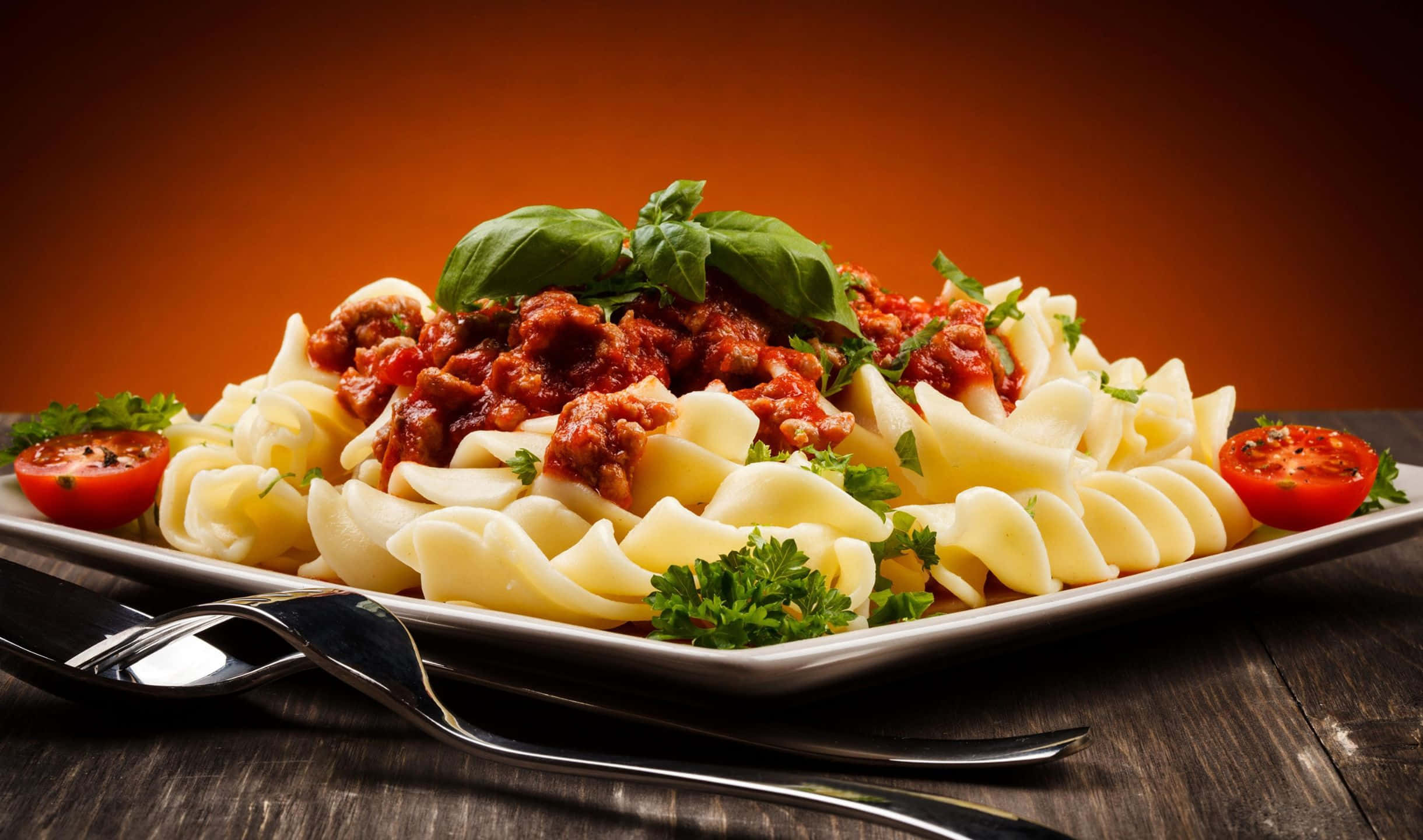 2440x1440 Pasta 桌布 壁紙 — 一盤寬條麵配濃郁肉醬，飾以羅勒和對半切開的櫻桃番茄，放在質樸的木桌上。
