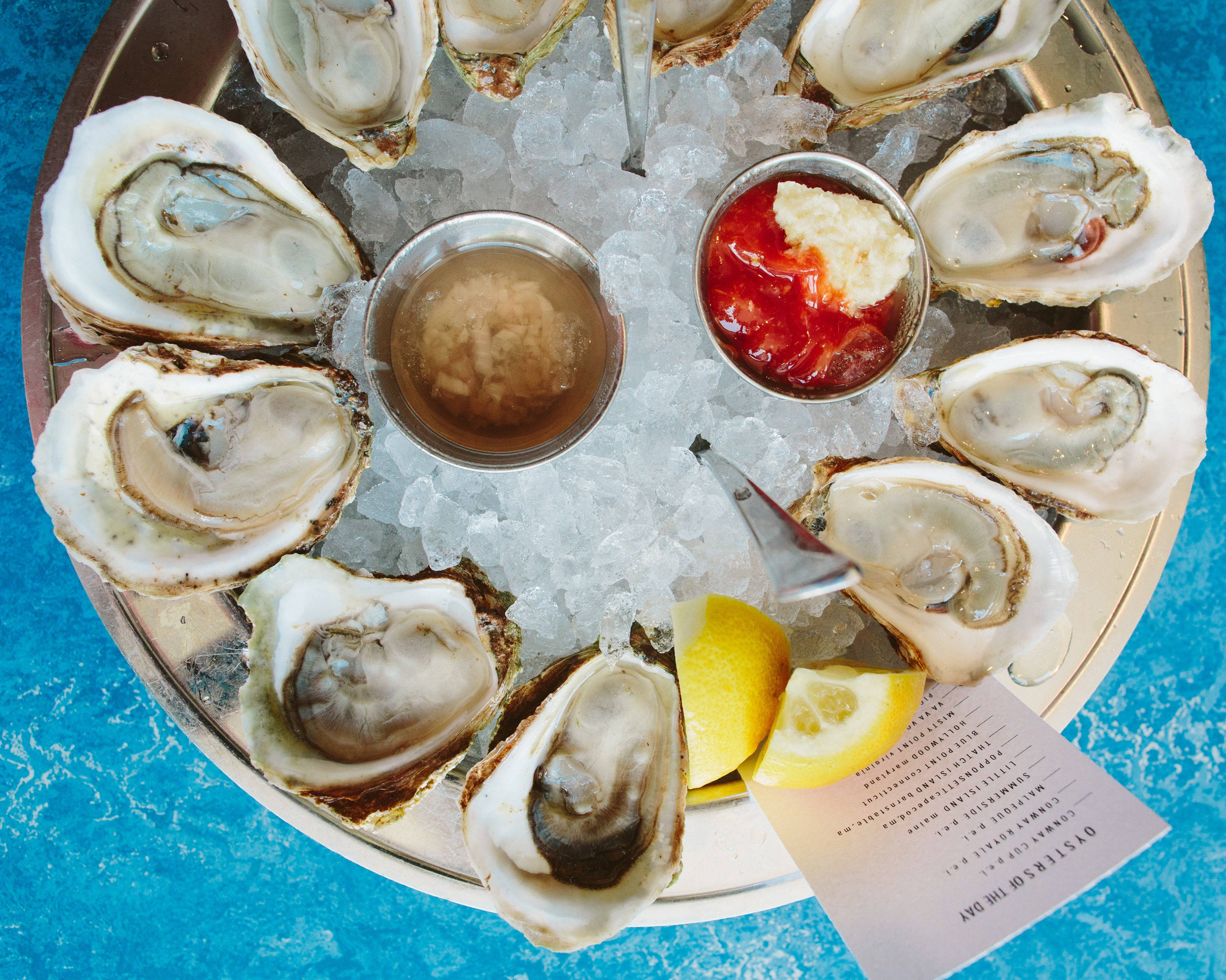 Seafood 桌布 壁紙 — 一盤新鮮生蠔放在碎冰上，搭配檸檬角和醬汁，擺放在充滿活力的藍色紋理表面上。