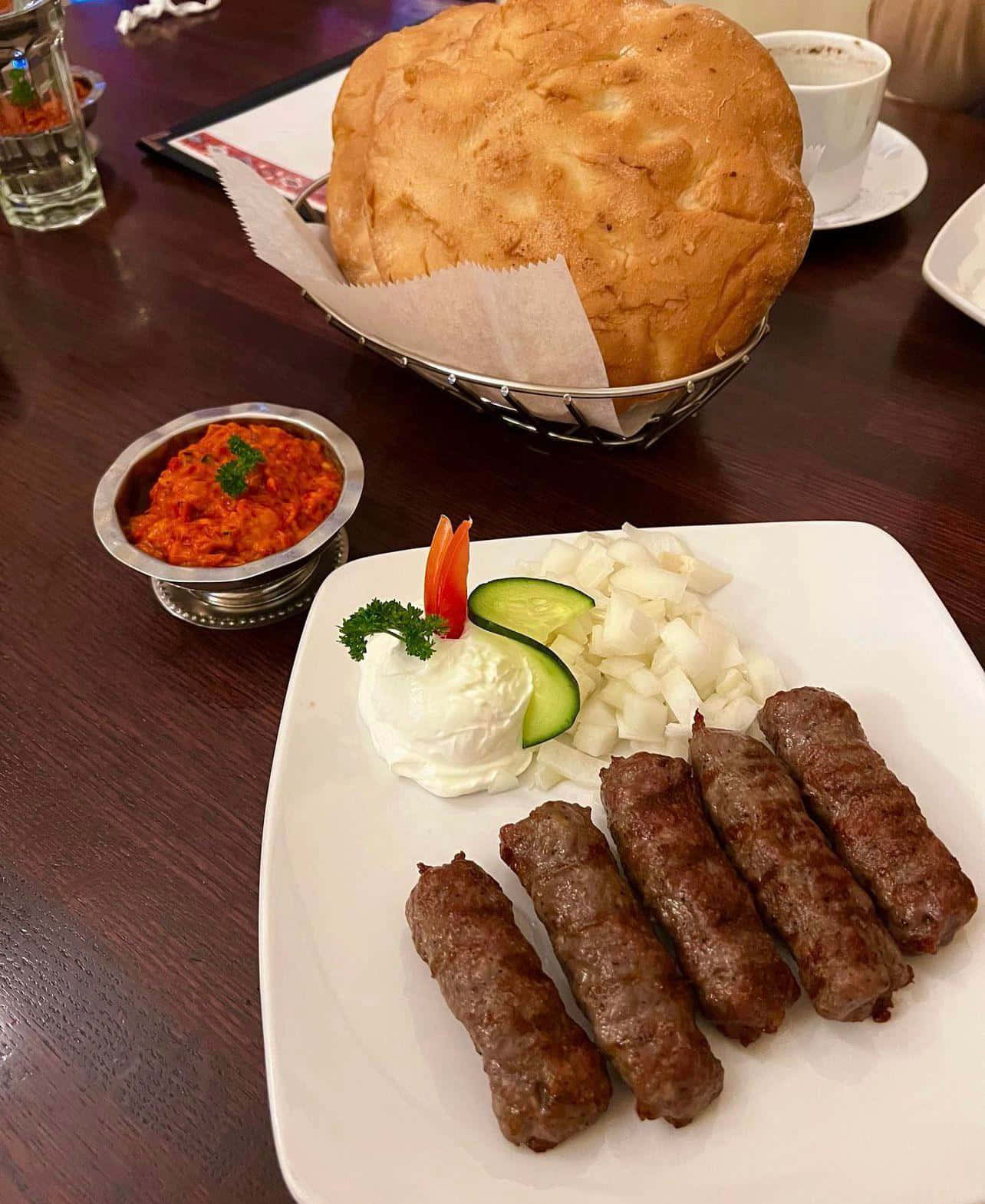 meat 桌布 壁紙 — 一盤烤香腸配優格黃瓜洋蔥裝飾，以及一個大金黃色麵包，放在深色木桌上。