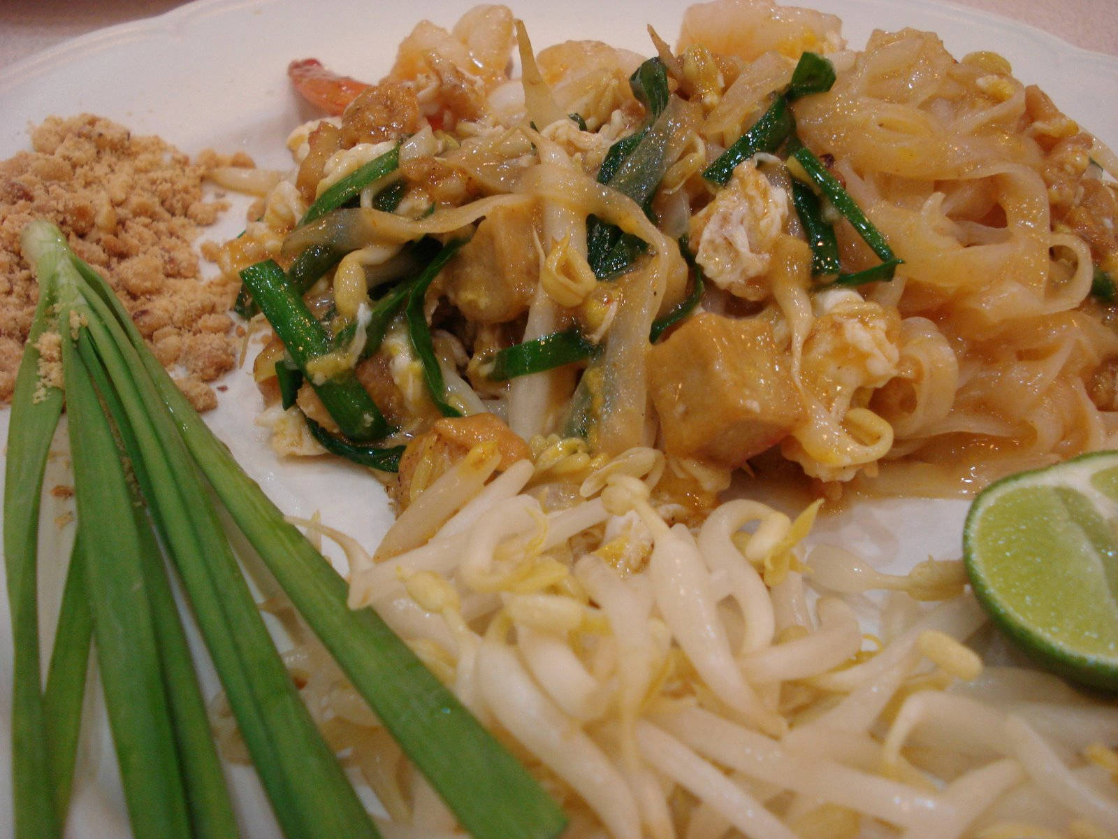 thai 桌布 壁紙 — 一盤熱騰騰的泰式炒河粉特寫，有蝦、豆腐、豆芽和青蔥，上面撒了碎花生和萊姆。