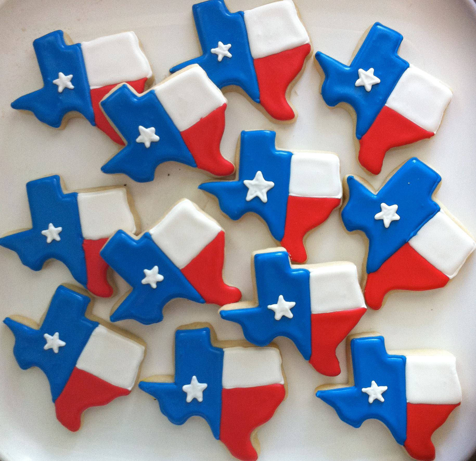 Texas Flag 桌布 壁紙 — 一盤精心裝飾的德州形狀餅乾，帶有藍色、白色和紅色的糖霜以及一顆白色的星星。