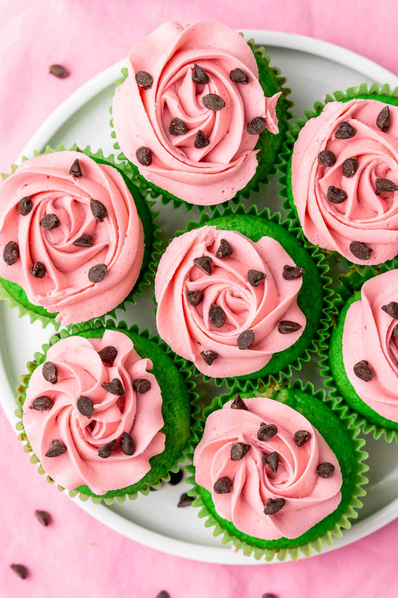 Pink Cupcakes 桌布 壁紙 — 一盤綠色紙杯蛋糕，上面有粉紅色玫瑰漩渦糖霜和巧克力碎，放在粉紅色背景上。