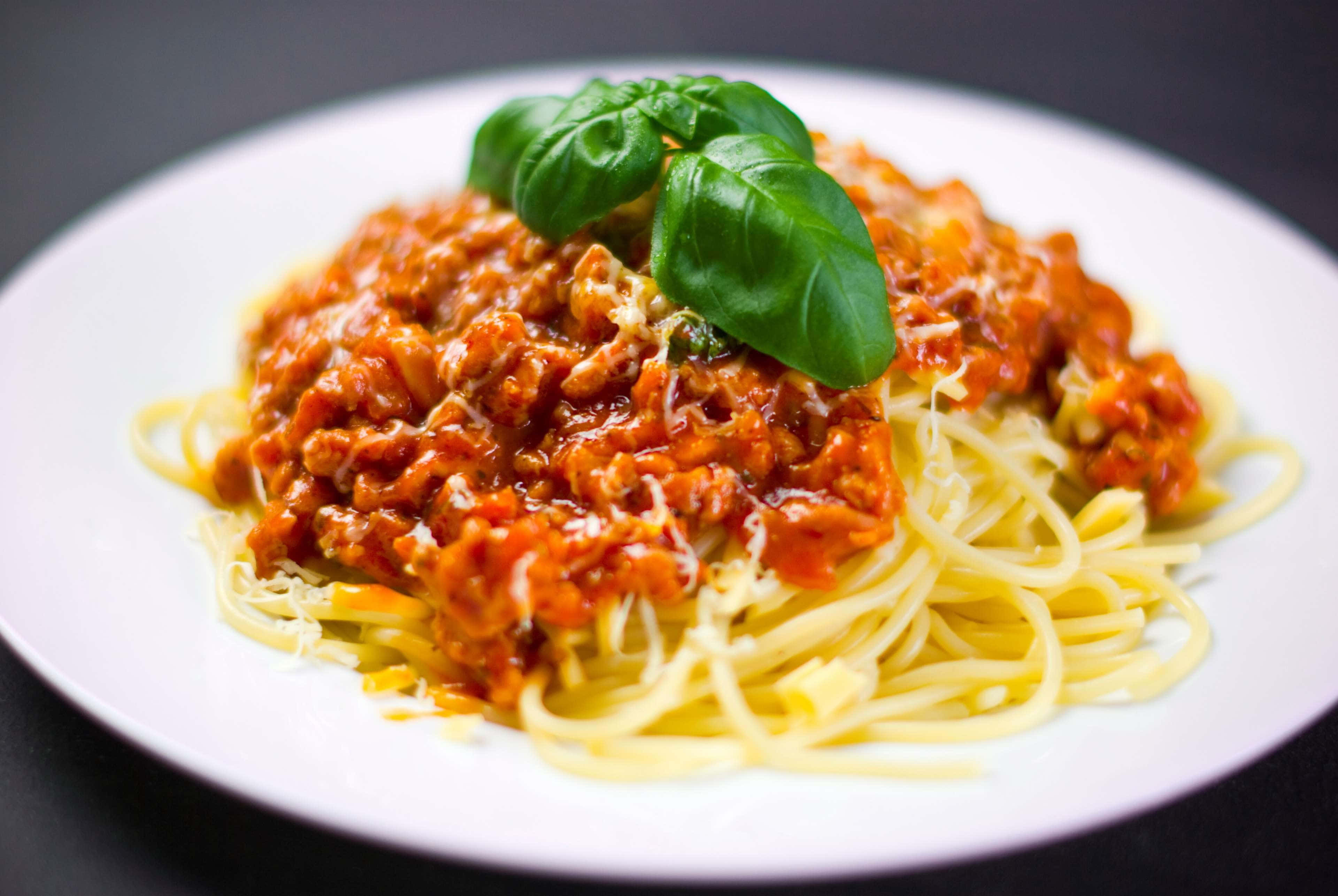 Spaghetti 桌布 壁紙 — 一盤義大利麵配上濃郁肉醬和新鮮羅勒葉裝飾。