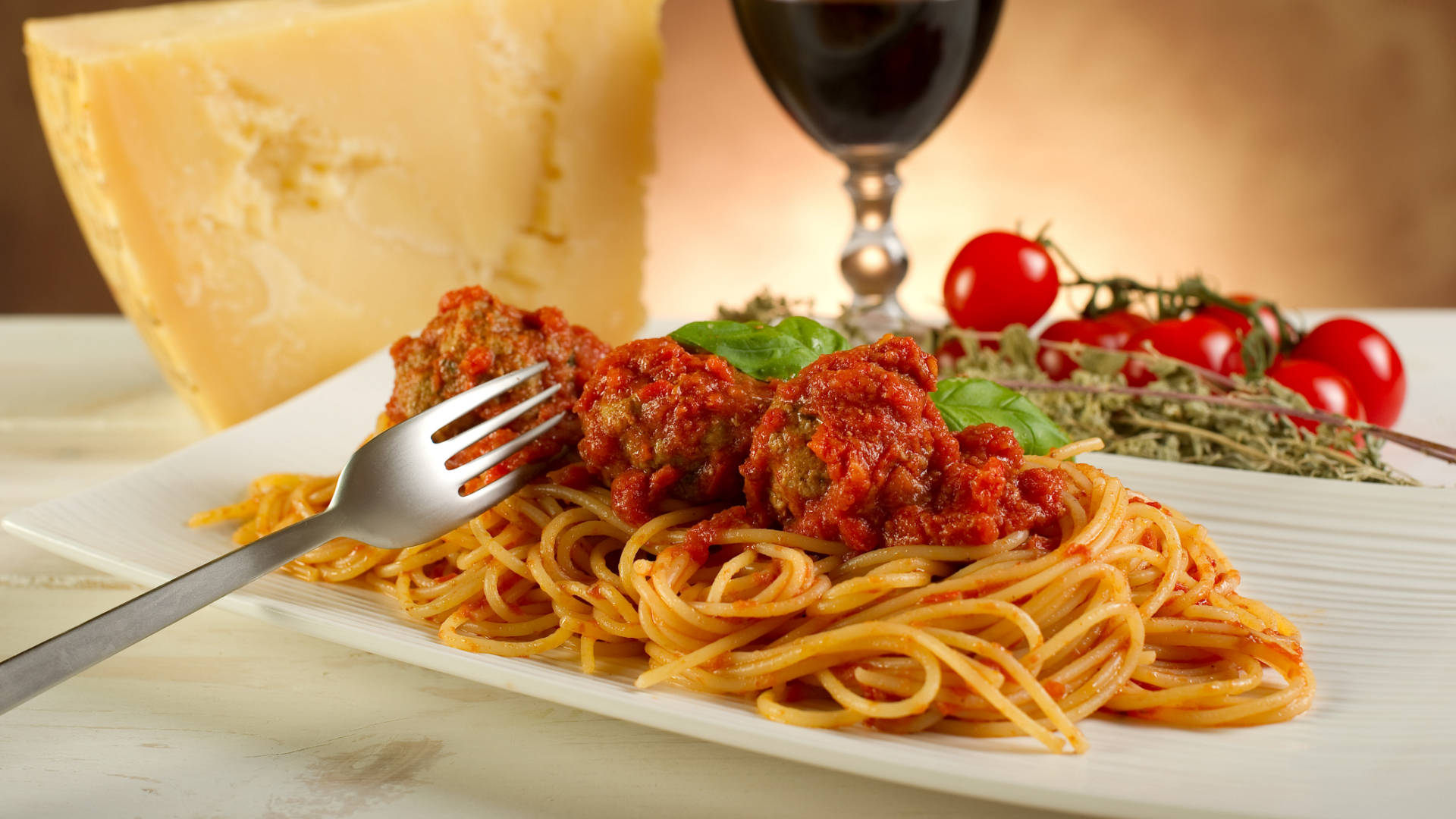 Pasta 桌布 壁紙 — 一盤義大利麵配肉丸和番茄醬，飾以羅勒和櫻桃番茄，旁邊有一杯紅酒和一塊帕瑪森起司。