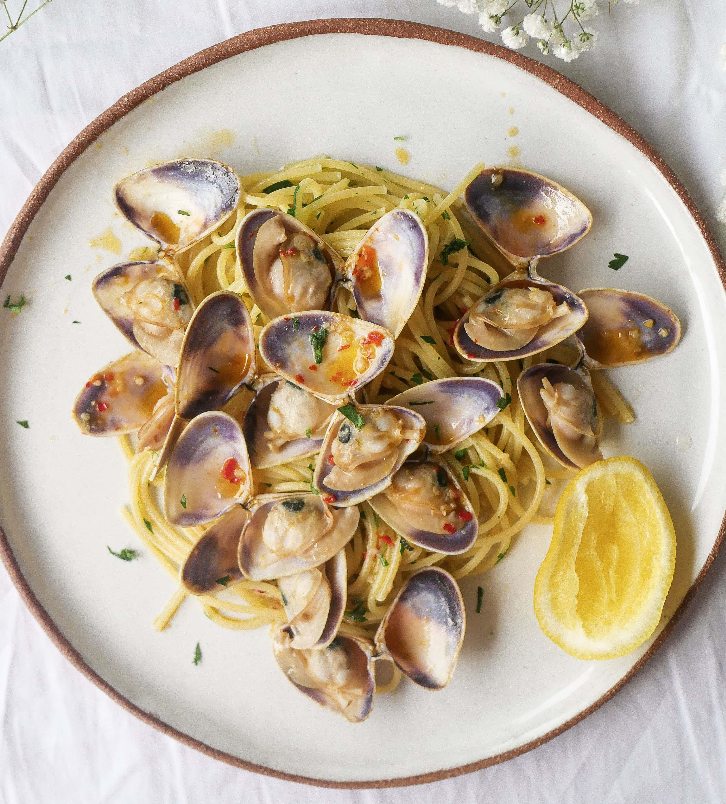 Clam 桌布 壁紙 — 一盤義大利麵配蛤蜊，飾以歐芹和辣椒油，伴以檸檬角放在白布上。