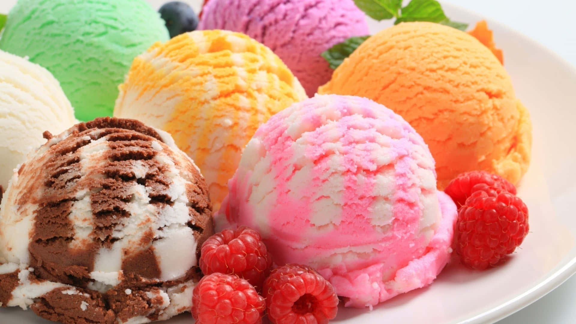Ice Cream 桌布 壁紙 — 一盤色彩繽紛的各種冰淇淋球，配上新鮮覆盆子和薄荷葉作點綴。