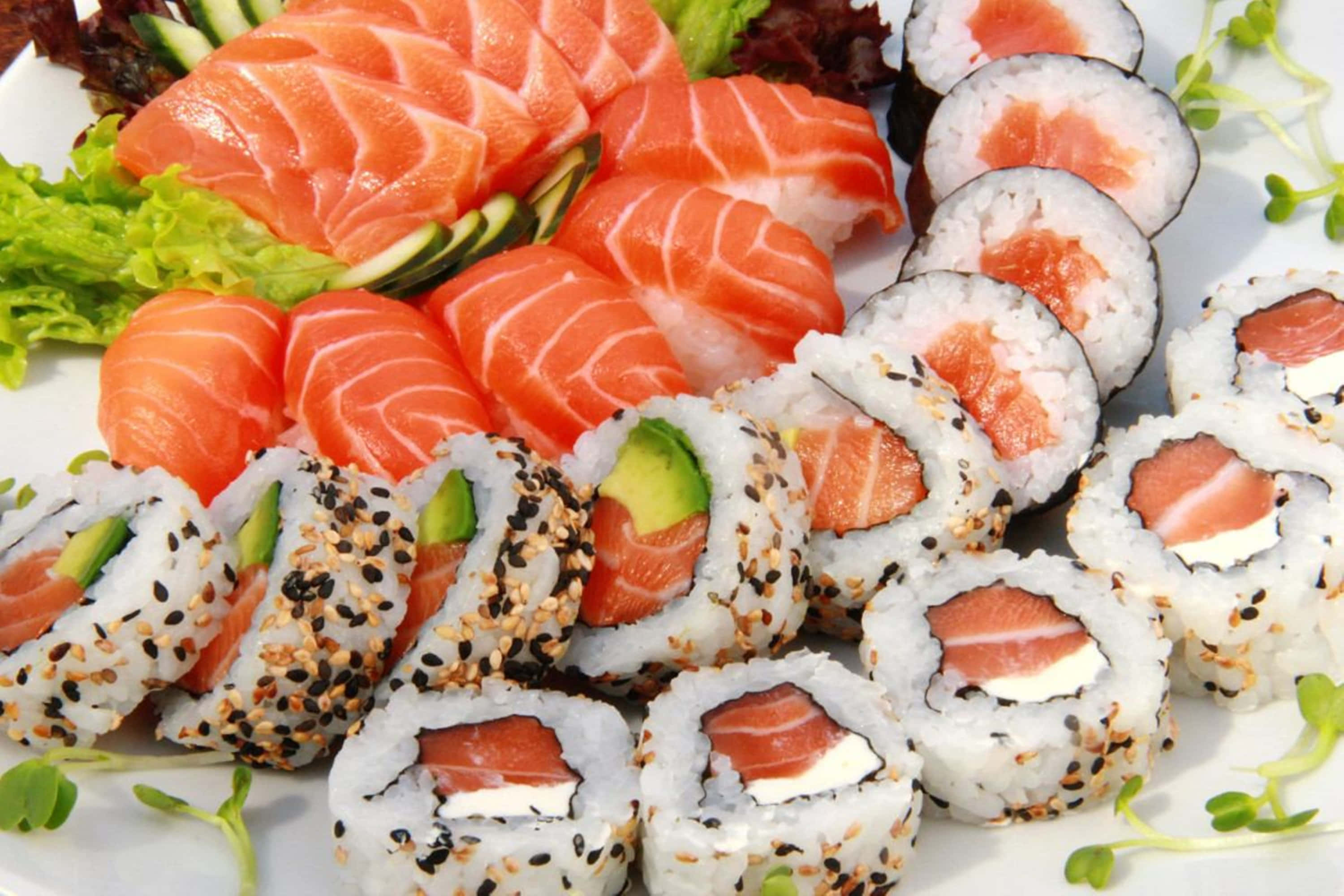 Sushi 桌布 壁紙 — 一盤色彩繽紛的新鮮壽司，包括鮭魚刺身和各式卷物，上面撒有芝麻和酪梨。
