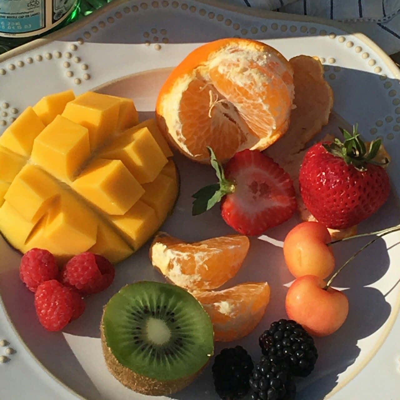 Aesthetic Food 桌布 壁紙 — 一盤色彩繽紛的新鮮水果，包括芒果、奇異果、草莓和櫻桃，沐浴在溫暖的陽光下。