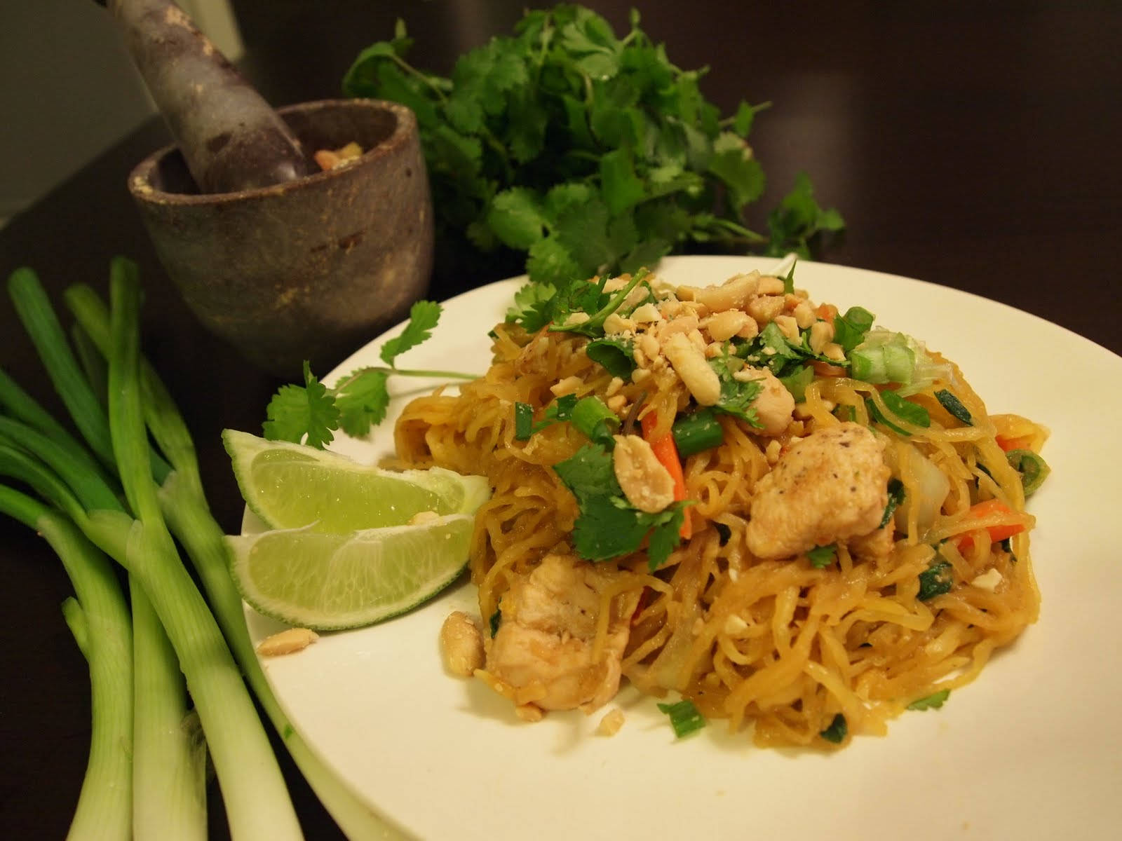 thai 桌布 壁紙 — 一盤色彩繽紛的泰式雞肉炒河粉，上面撒有花生、香菜和萊姆角，旁邊放有新鮮青蔥和一個石臼。