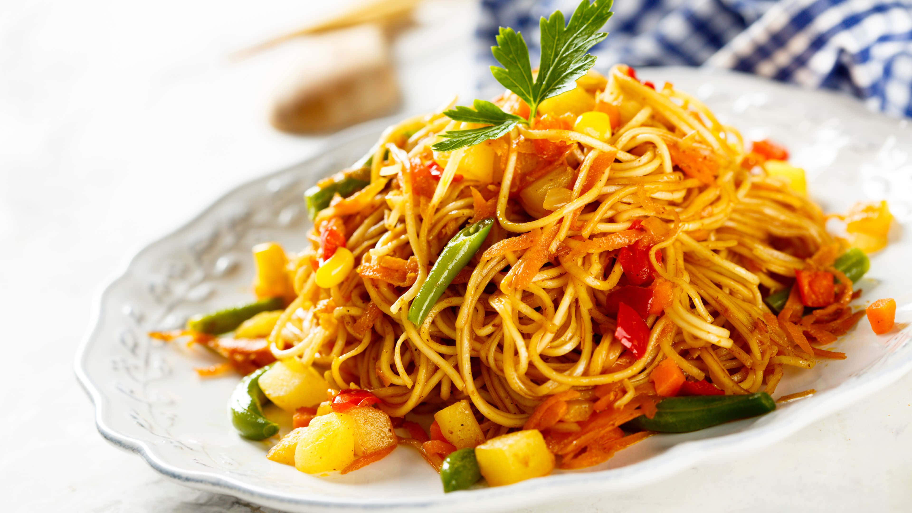 Noodles 桌布 壁紙 — 一盤色彩繽紛的炒麵，配上鮮豔蔬菜和歐芹裝飾，盛放在精緻的白色盤子上。