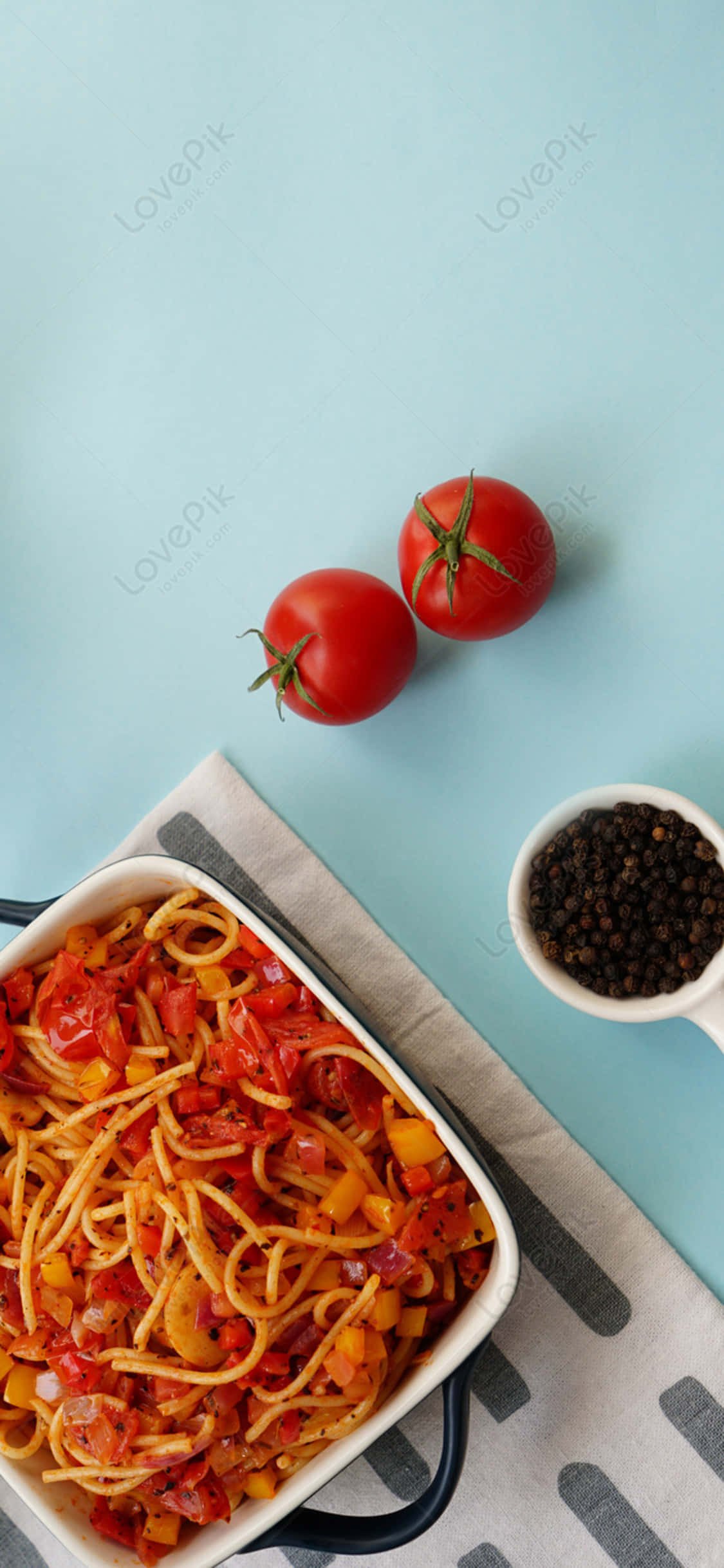 food iPhone 桌布 壁紙 — 一盤色彩繽紛的義大利麵配番茄醬和甜椒，放在白色烤盤中，旁邊是新鮮番茄和黑胡椒粒，置於淺藍色表面上。