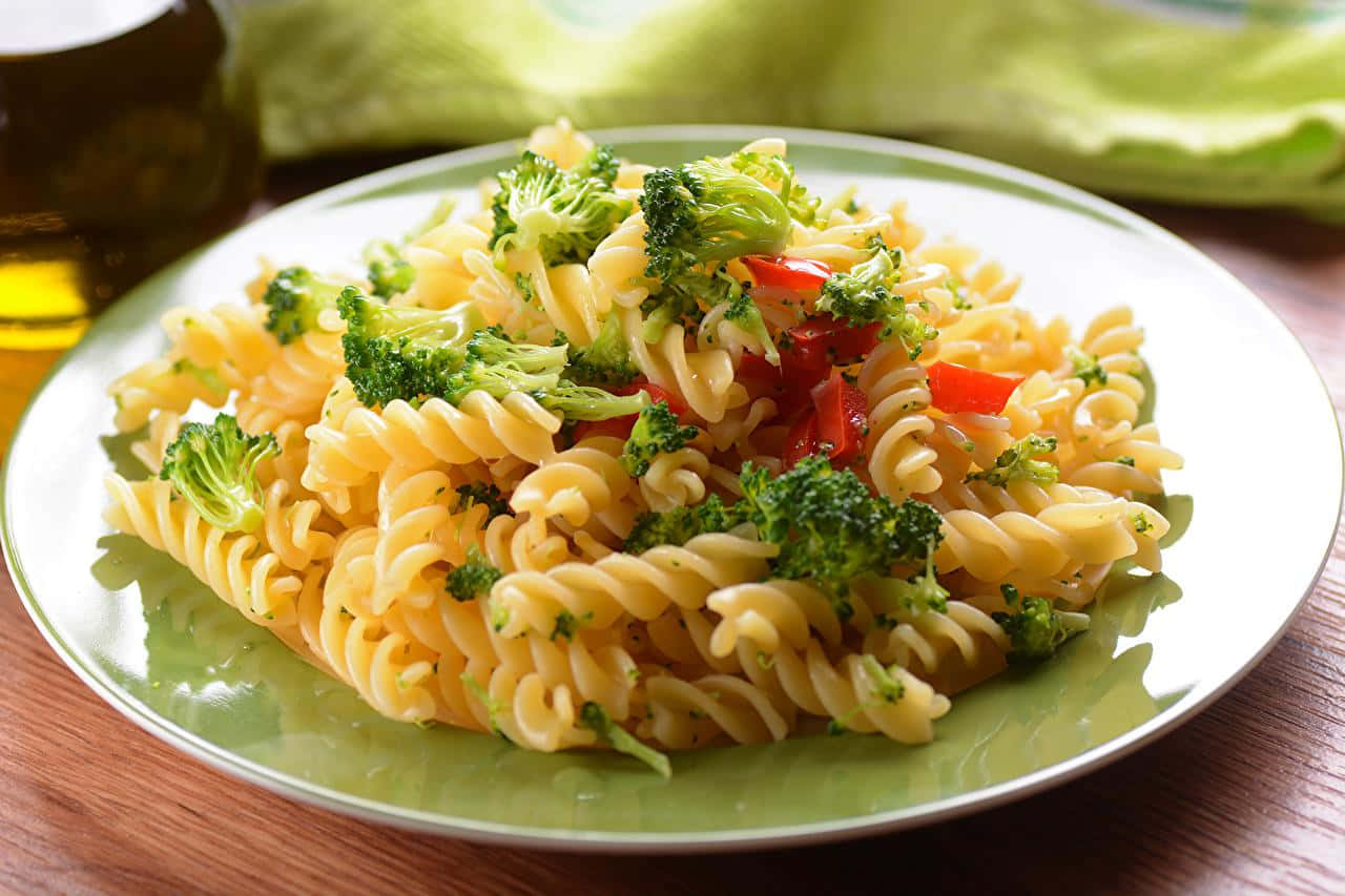 Pasta 桌布 壁紙 — 一盤色彩繽紛的螺旋義大利麵，上面鋪滿新鮮青花菜和紅甜椒，放在木桌上。