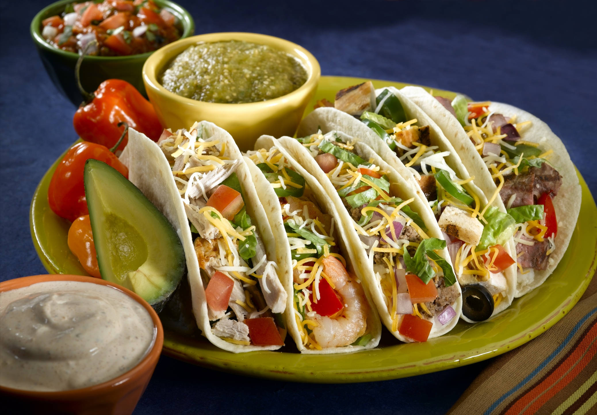 Mexican Food 桌布 壁紙 — 一盤色彩繽紛的軟玉米餅，內餡有蝦、雞肉和牛肉，上面鋪滿起司、番茄和生菜，周圍是新鮮莎莎醬、酪梨醬和各種醬汁。