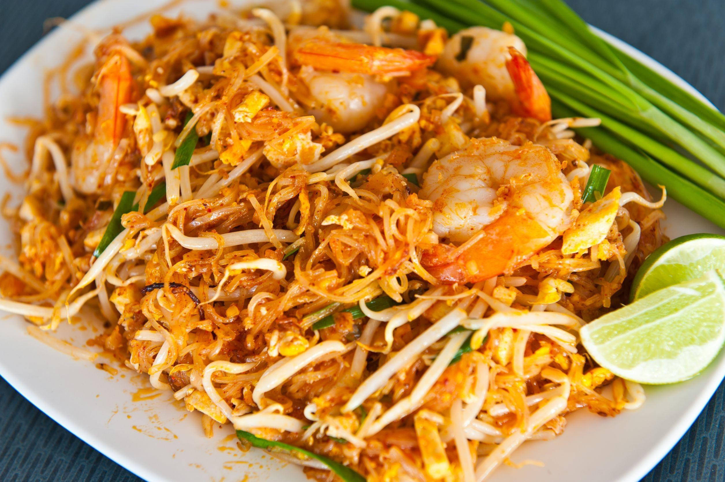 thai 桌布 壁紙 — 一盤色彩鮮豔的泰式炒金邊粉，搭配蝦仁、豆芽和萊姆裝飾。