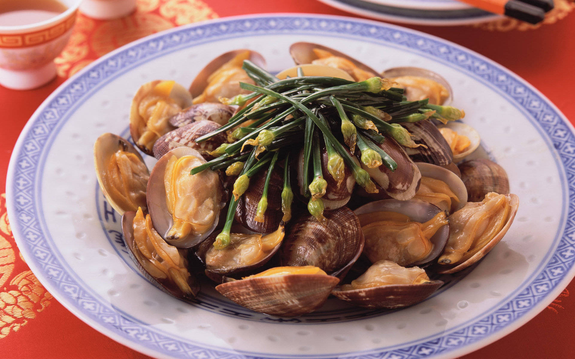 4K Food 桌布 壁紙 — 一盤蒸蛤蜊，上面放著青蔥，放在紅色桌布上，搭配圖案瓷器。