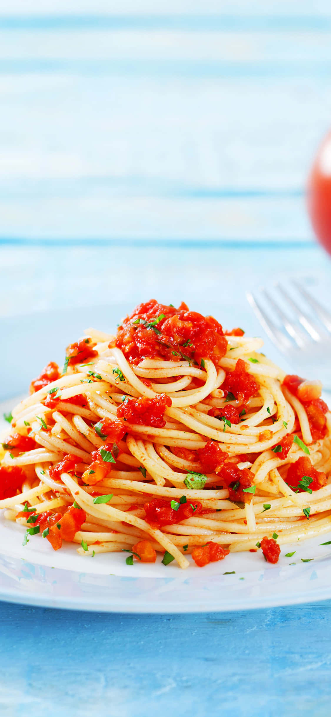 Spaghetti 桌布 壁紙 — 一盤誘人的義大利麵，配上濃郁的番茄醬和新鮮香草，放在白色盤子上，背景是柔和的藍色木質桌面。