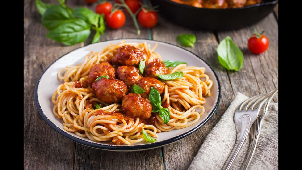 720p Pasta 桌布 壁紙 — 一盤鄉村風格的義大利麵配肉丸和新鮮羅勒，放在一張風化的木桌上，旁邊有櫻桃番茄和叉子。