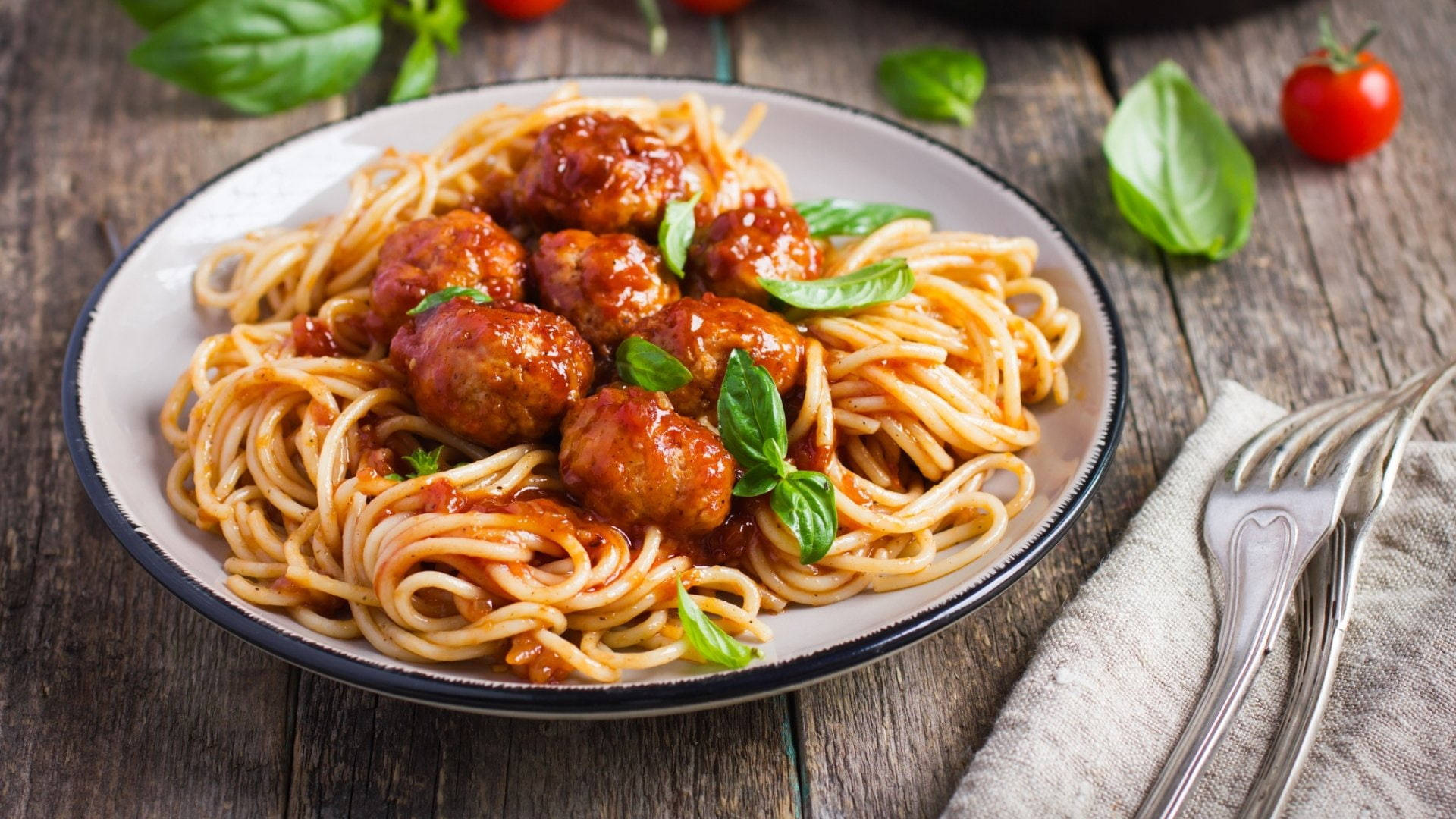 Pasta 桌布 壁紙 — 一盤鄉村風格的義大利麵配肉丸和新鮮羅勒，放在一張風化的木桌上，旁邊有叉子和櫻桃番茄。