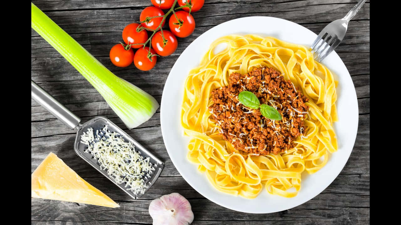 720p Pasta 桌布 壁紙 — 一盤配有濃郁肉醬、以羅勒和碎起司裝飾的寬條麵，旁邊放著新鮮番茄、芹菜、大蒜和起司，置於鄉村風木桌上。