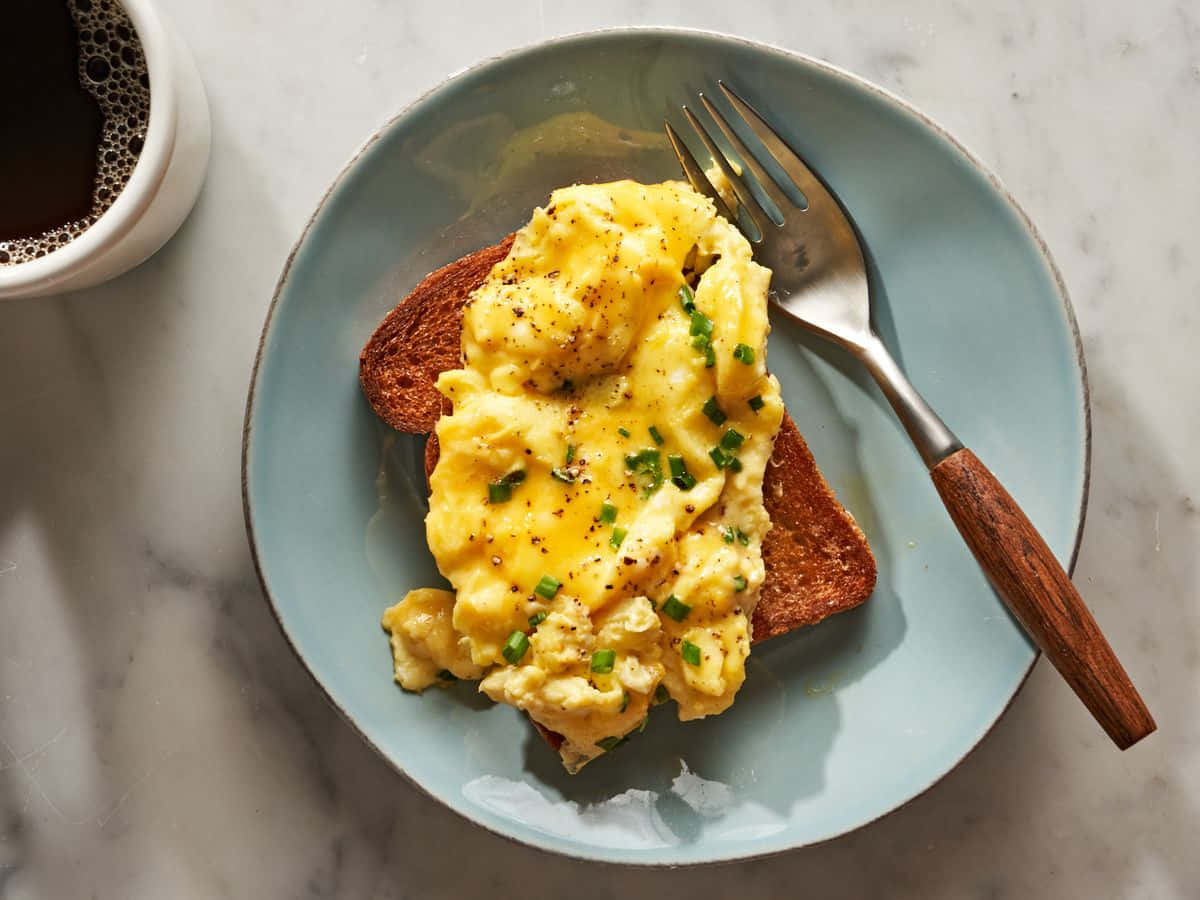 Scrambled Egg 桌布 壁紙 — 一盤鬆軟炒蛋佐細香蔥和胡椒，放在吐司上，旁邊有一杯咖啡，置於大理石表面。