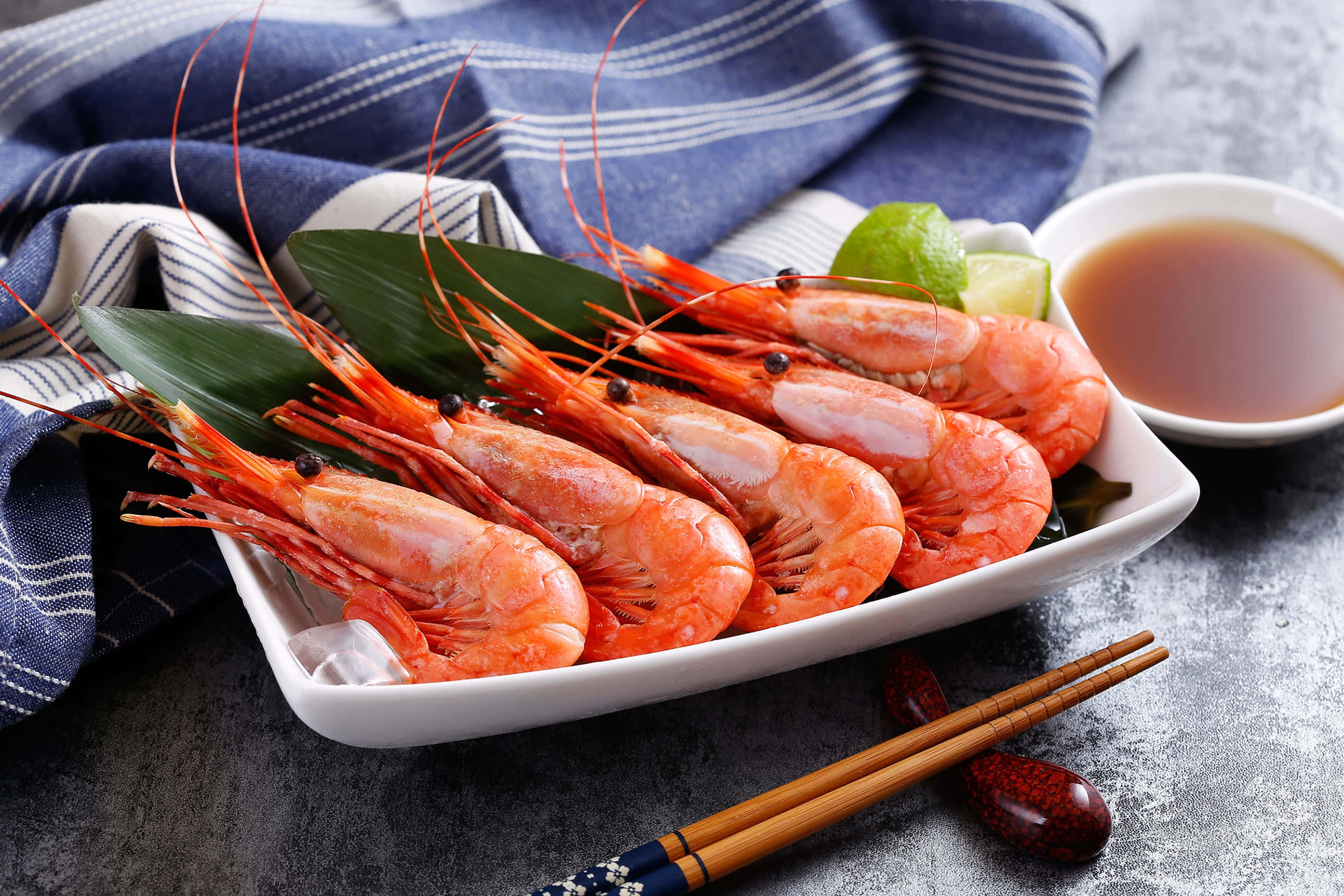 Seafood 桌布 壁紙 — 一盤鮮橙色熟蝦，以綠葉、萊姆和醬油點綴，放置在紋理灰色表面上。