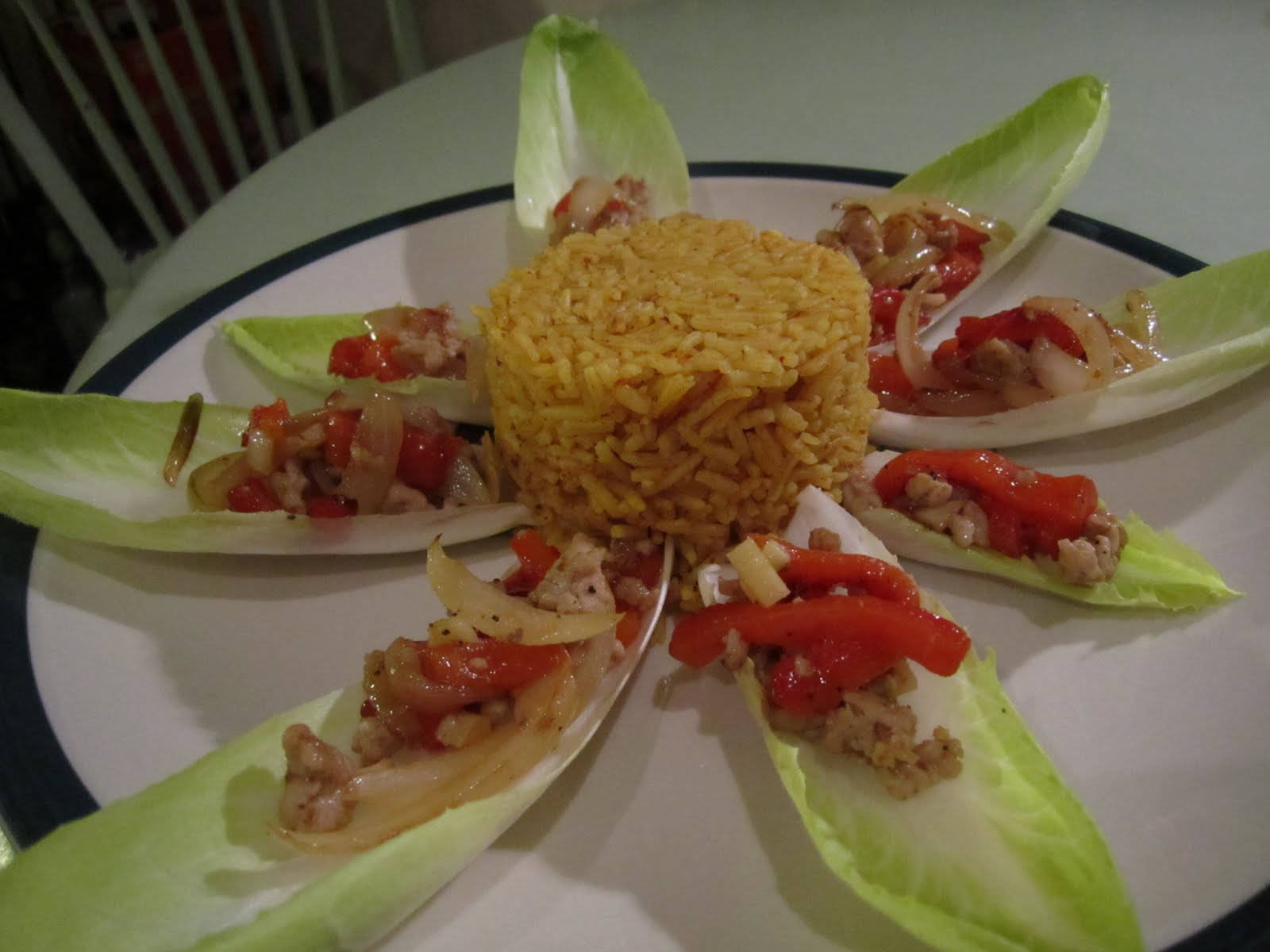 Delicious Food 桌布 壁紙 — 一盤鮮豔的黃色米飯，中央圍繞著一圈菊苣葉，裡面填滿了美味的肉和紅椒混合物。