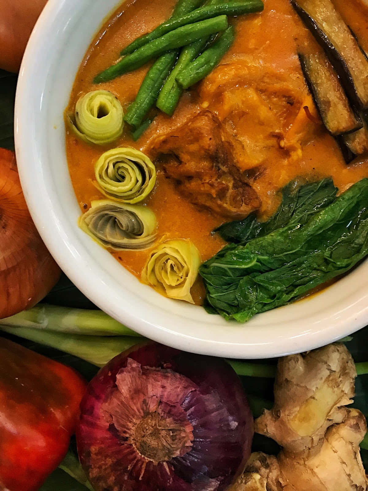 meat 桌布 壁紙 — 一碗充滿活力的濃郁橙色咖哩，配有青豆、朝鮮薊心和菠菜，周圍是新鮮的整粒香料。