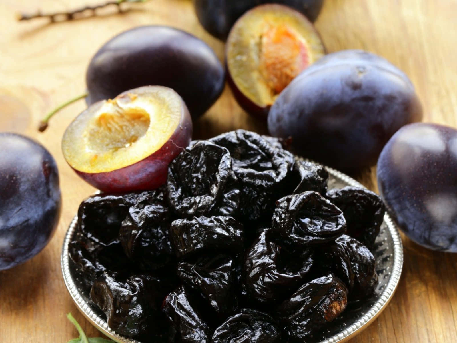 Fruits 桌布 壁紙 — 一碗光澤深色西梅乾放在溫暖的木質表面上，旁邊是新鮮的紫色李子。