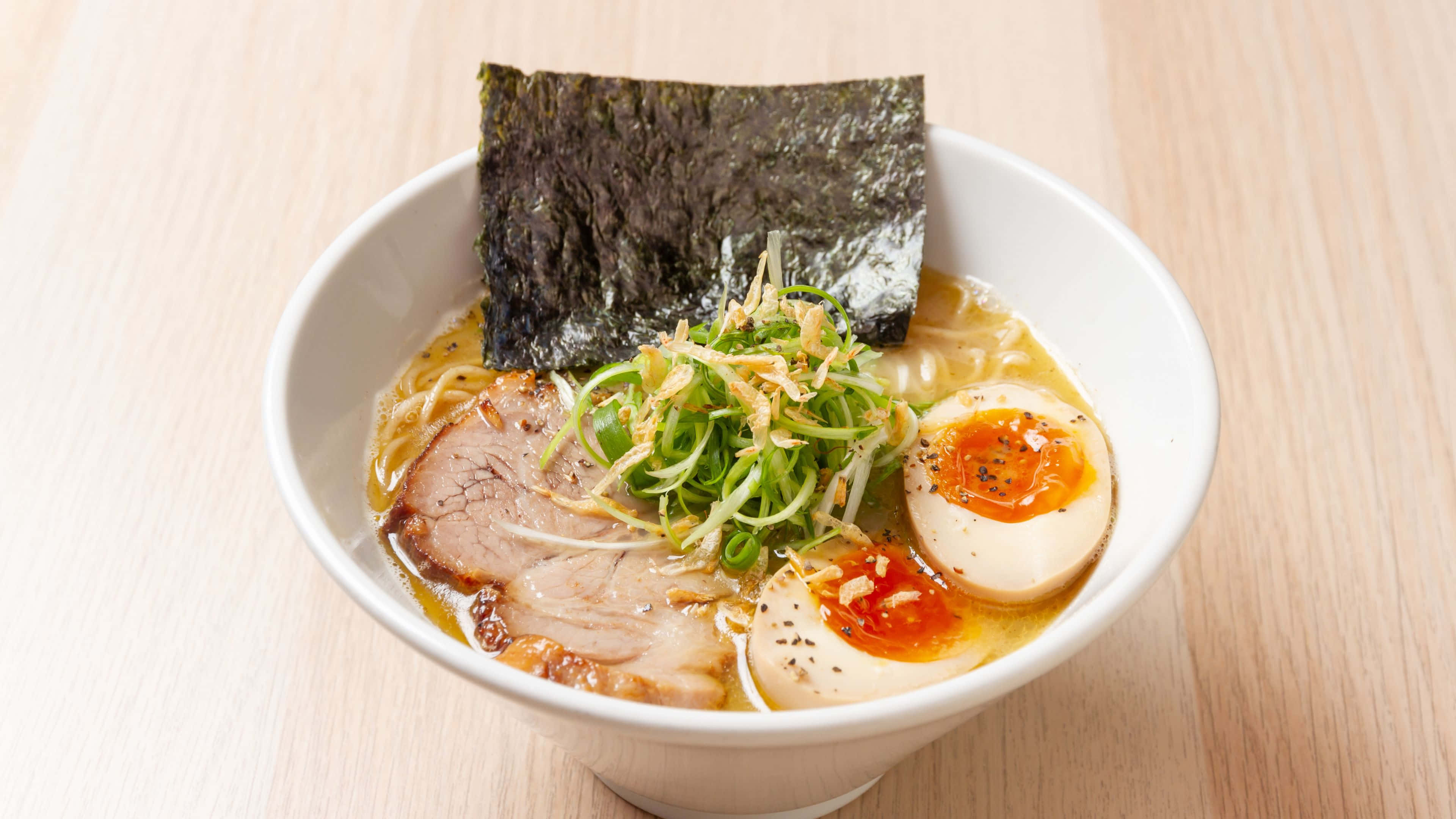 Noodles 桌布 壁紙 — 一碗冒煙的拉麵，有溏心蛋、海苔和叉燒，放在淺色木桌上。