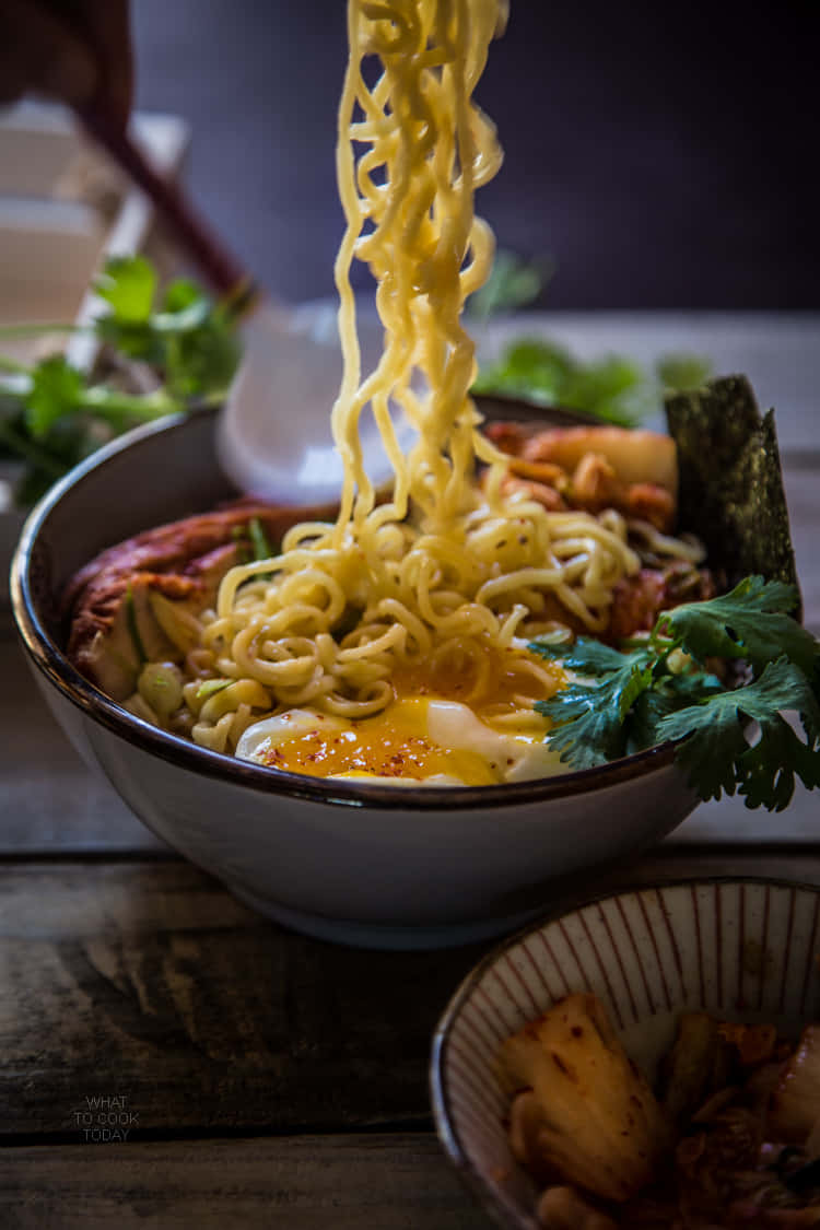 Noodles 桌布 壁紙 — 一碗冒煙的拉麵，筷子夾起麵條，露出半熟蛋和新鮮香菜。
