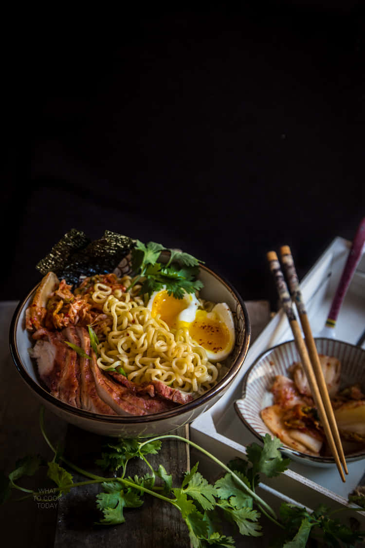 Noodles 桌布 壁紙 — 一碗冒煙的拉麵，配有半熟蛋、培根、泡菜和香菜，放在深色木桌上。