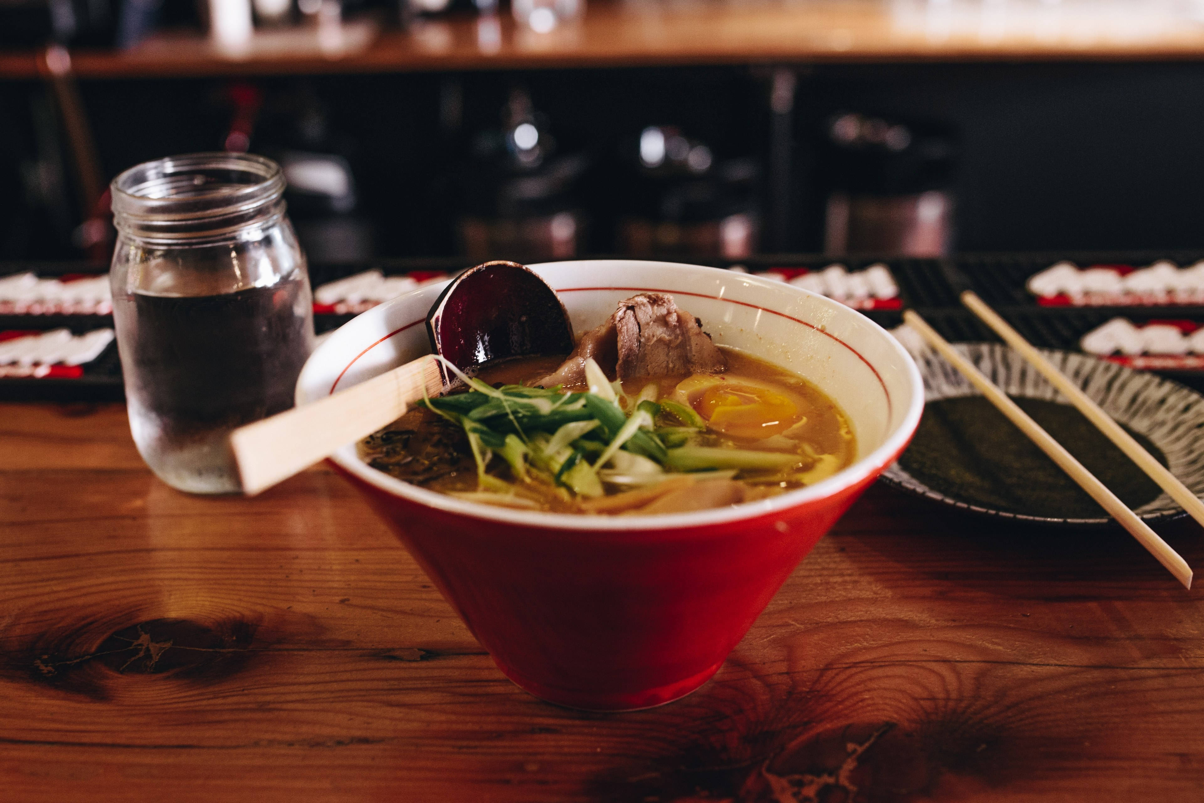 bowl 桌布 壁紙 — 一碗冒煙的拉麵，配有半熟蛋和叉燒，放在質樸的木桌上，旁邊有筷子和一杯水。