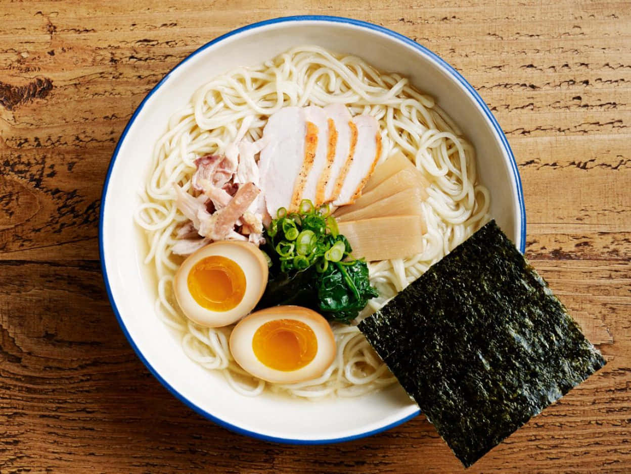 Noodles 桌布 壁紙 — 一碗冒煙的拉麵，配有溏心蛋、切片豬肉、青蔥和海苔，放在質樸的木桌上。