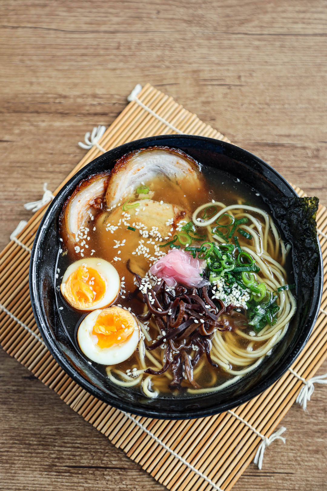 Food Photography 桌布 壁紙 — 一碗冒煙的拉麵，配有溏心蛋、叉燒豬肉、青蔥和芝麻，放在木桌上的竹蓆上。