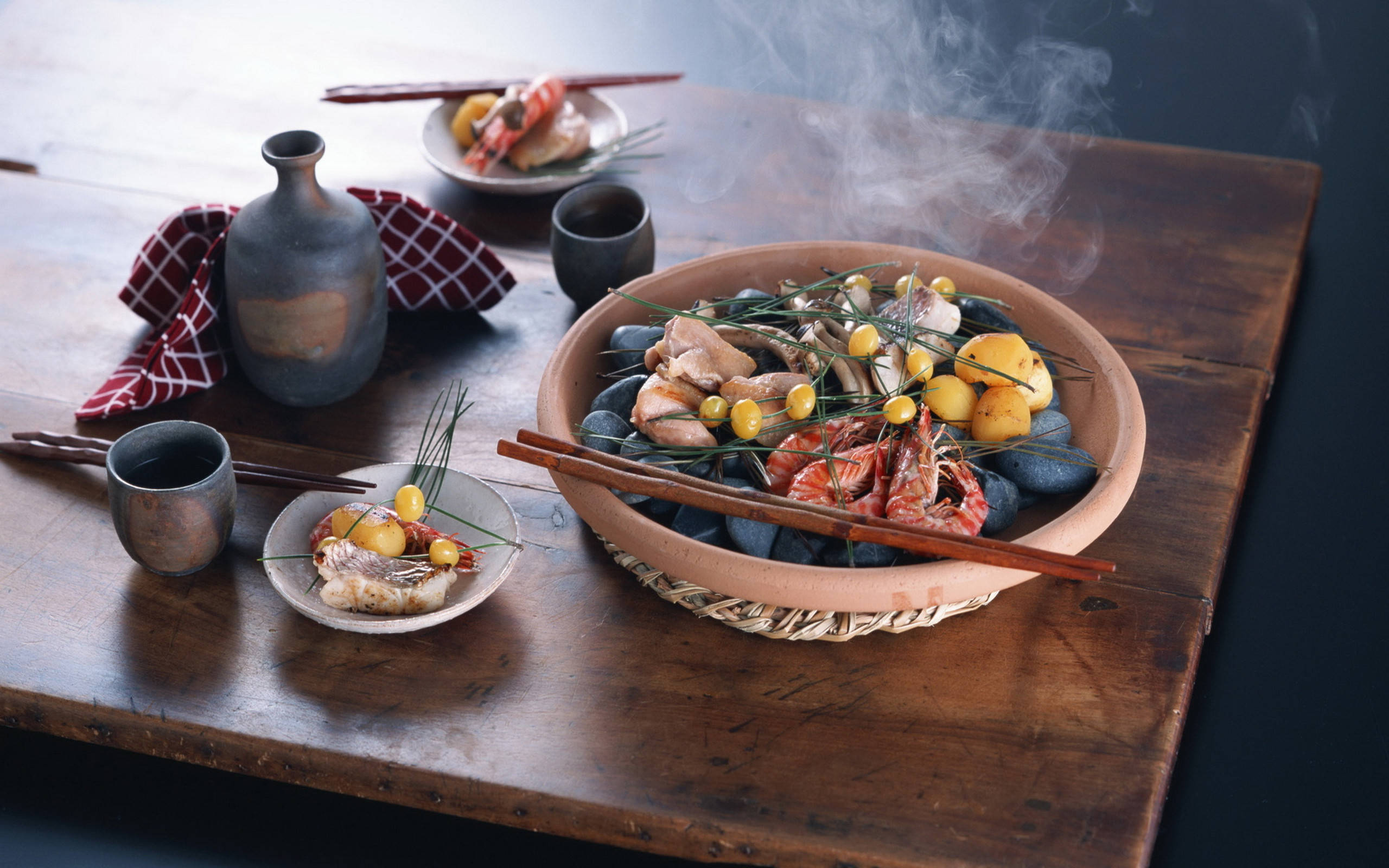 4K 食物 桌布 壁紙 — 一碗冒煙的海鮮和馬鈴薯放在熱石上，置於質樸的木桌上，搭配陶瓷杯和筷子。