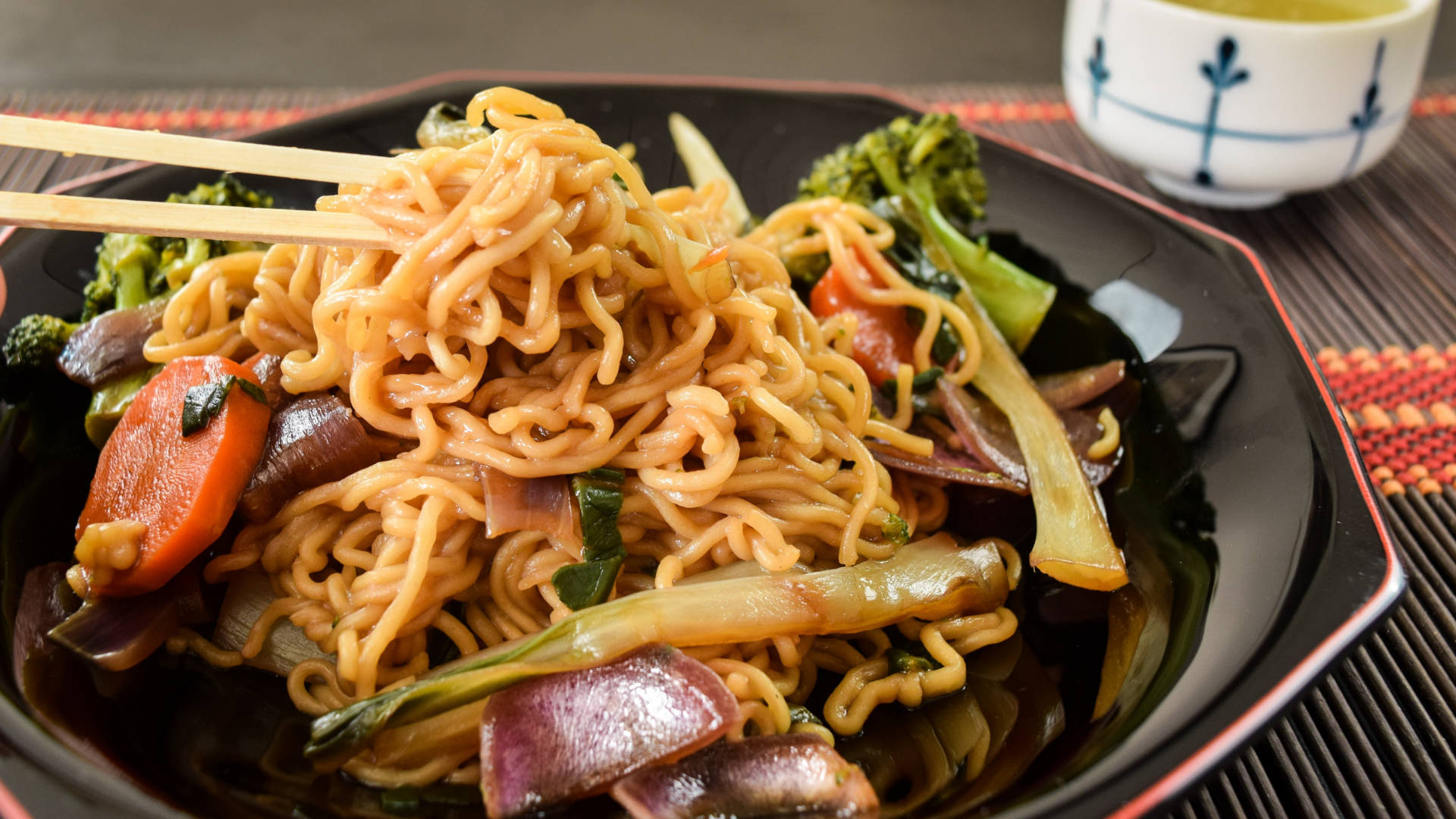 Pasta 桌布 壁紙 — 一碗冒煙的炒麵，搭配色彩繽紛的蔬菜，筷子夾起一部分。