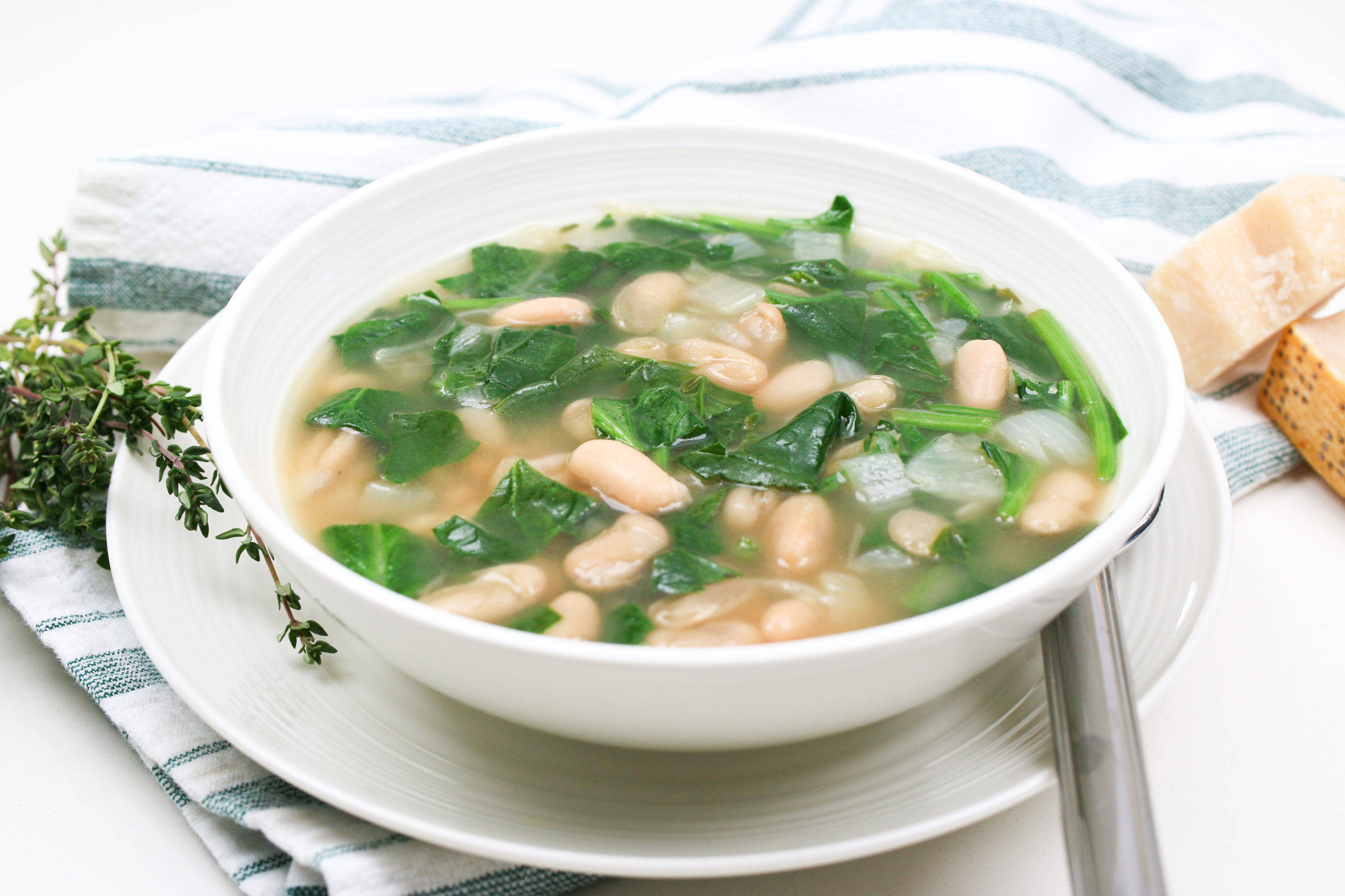 beans 桌布 壁紙 — 一碗冒煙的白豆菠菜湯放在條紋布上，旁邊有新鮮百里香和起司。