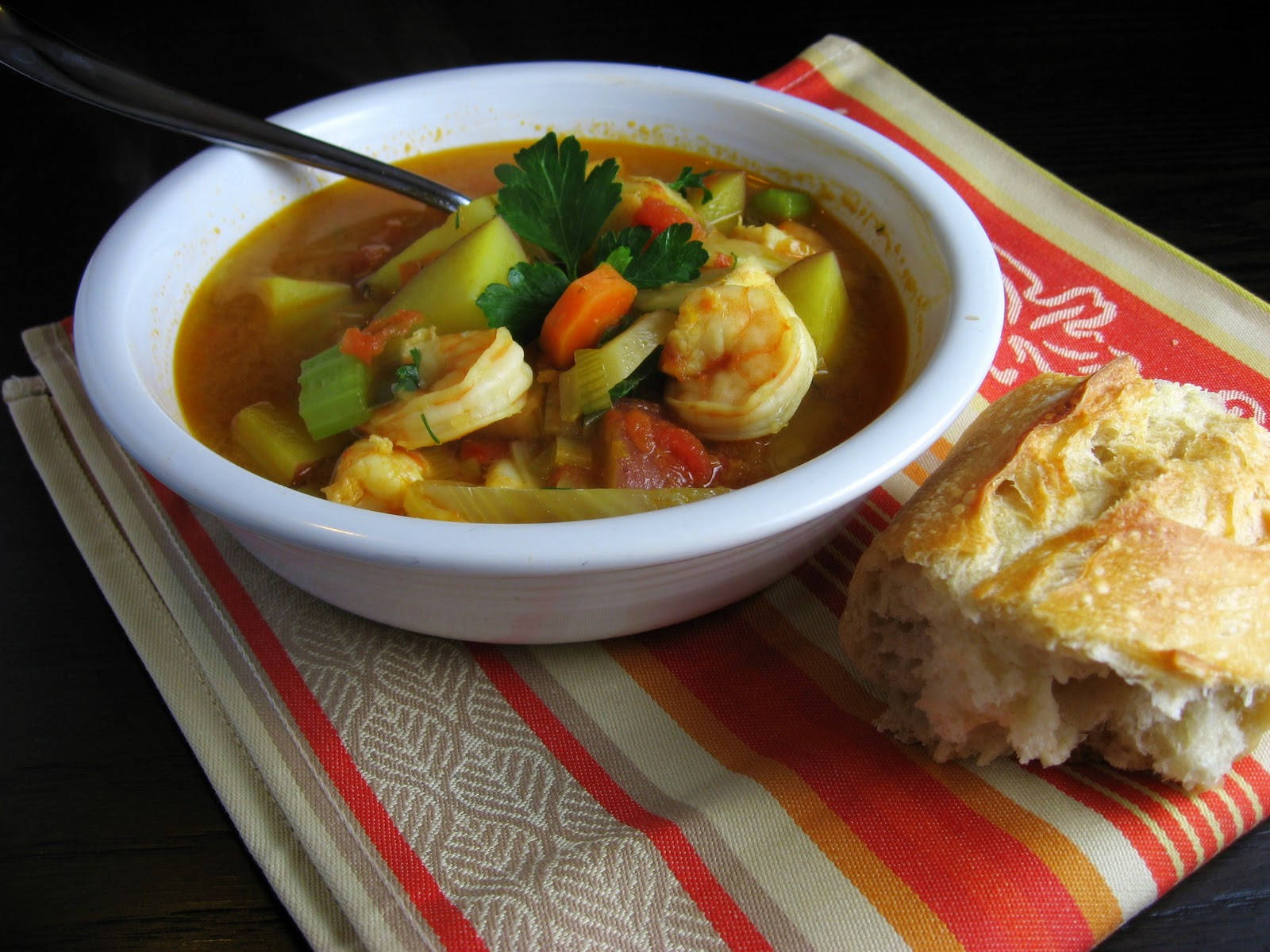 Delicious Food 桌布 壁紙 — 一碗冒煙的蝦和蔬菜湯，飾以歐芹，旁邊放著一個脆皮麵包卷，放在條紋餐巾上。