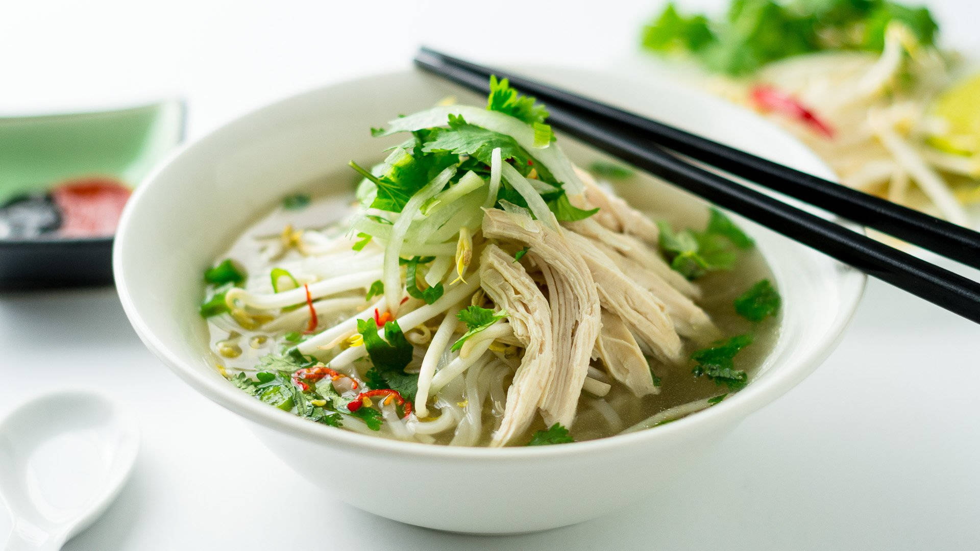 Vietnam 桌布 壁紙 — 一碗冒煙的越南河粉，配上嫩雞肉麵條、豆芽、香菜和辣椒裝飾，筷子擱在碗邊。