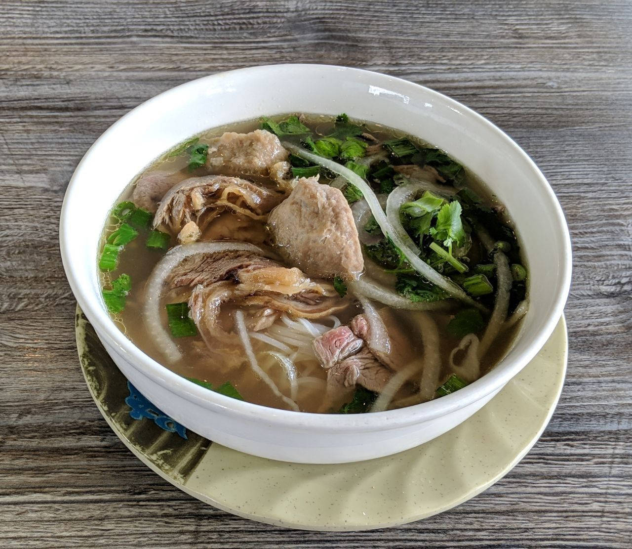 bowl 桌布 壁紙 — 一碗冒煙的越南河粉，配有嫩牛肉片、米粉和新鮮香草，放在木桌上。
