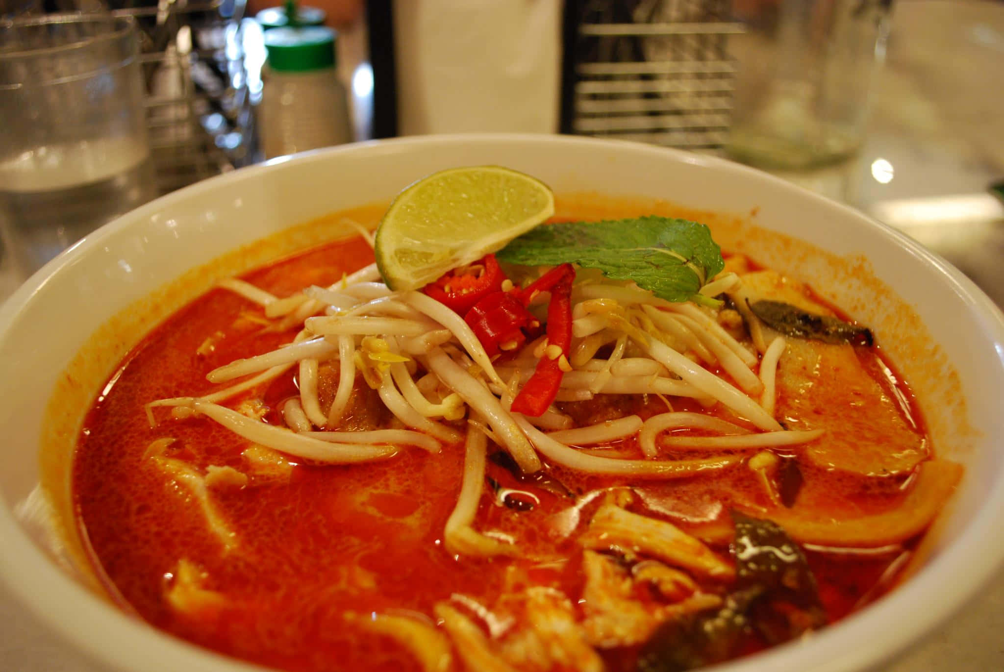 Noodles 桌布 壁紙 — 一碗冒煙的鮮紅色咖哩湯麵，上面放有豆芽、辣椒、萊姆和薄荷。