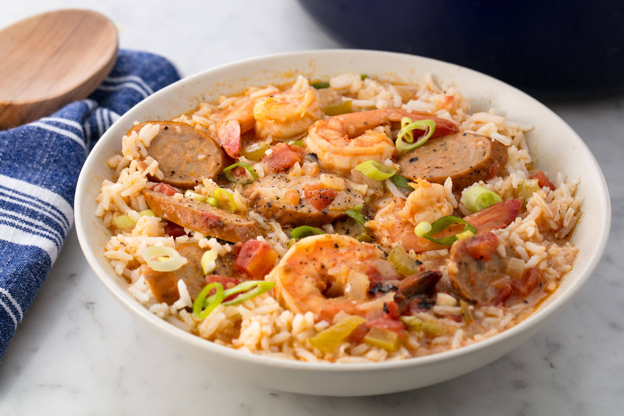 shrimp 桌布 壁紙 — 一碗冒著熱氣的什錦飯，有蝦、香腸和青蔥，放在大理石檯面上，旁邊有一條藍色條紋毛巾。
